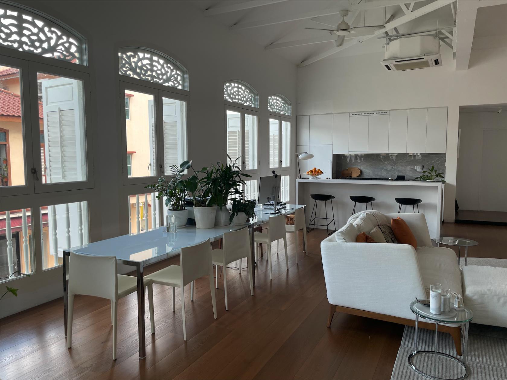 A photo studio with arched windows, wooden floors, potted plants, and an open kitchen at Modern Joo Chiat Shophouse.