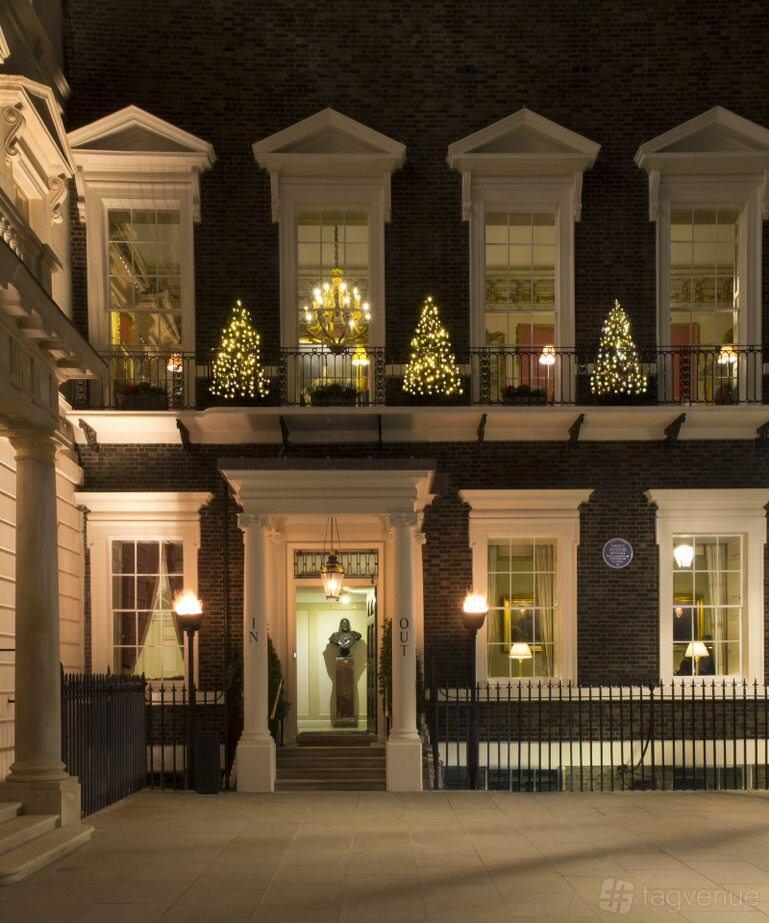 A historic building with illuminated Christmas trees on a balcony and a lit chandelier at In and Out (Naval & Military) Club.