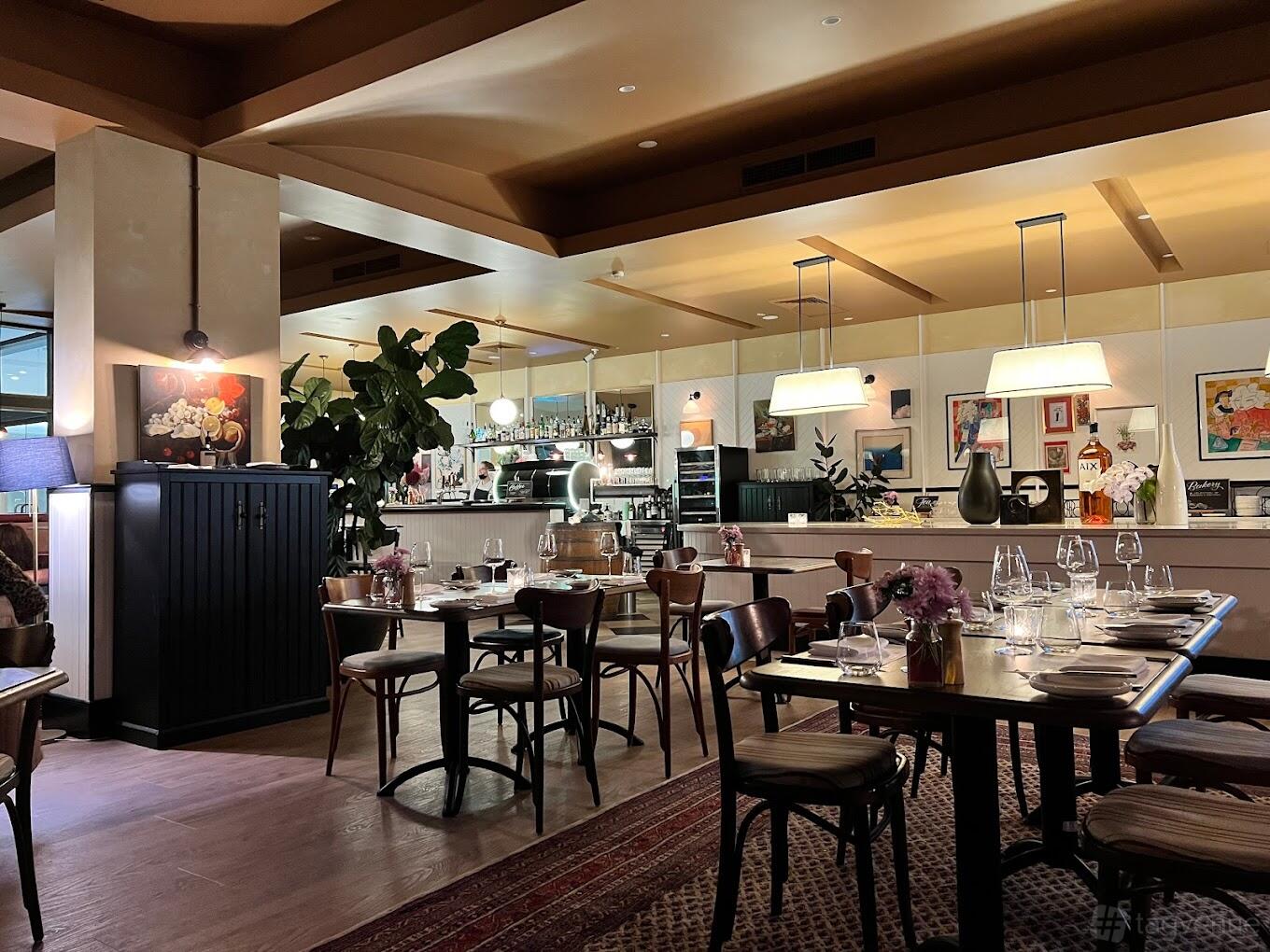 A restaurant with wooden tables set with glassware, pendant lighting, and eclectic wall art at Bistro Manly.