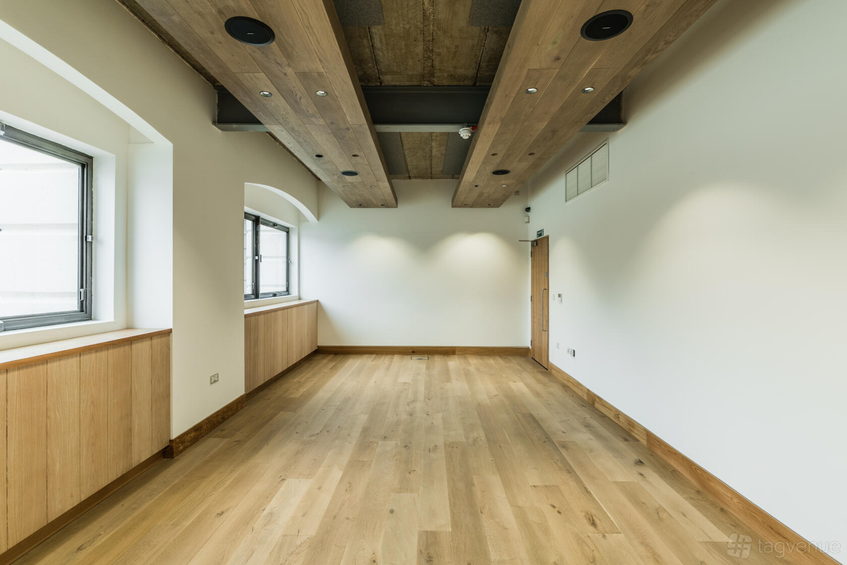 A hall with large windows, wood-paneled flooring, and exposed wooden ceiling beams at Glaziers Hall Limited.