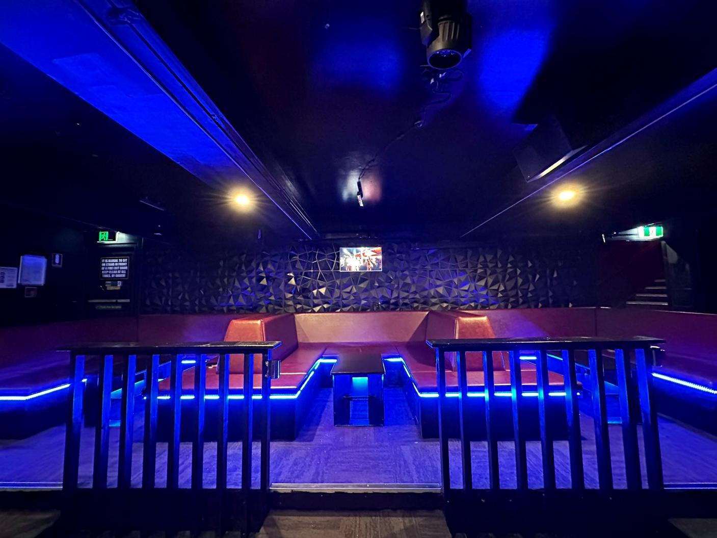 A nightclub dining room with red leather booth seating, geometric textured walls, and blue accent lighting at Mi Casa.