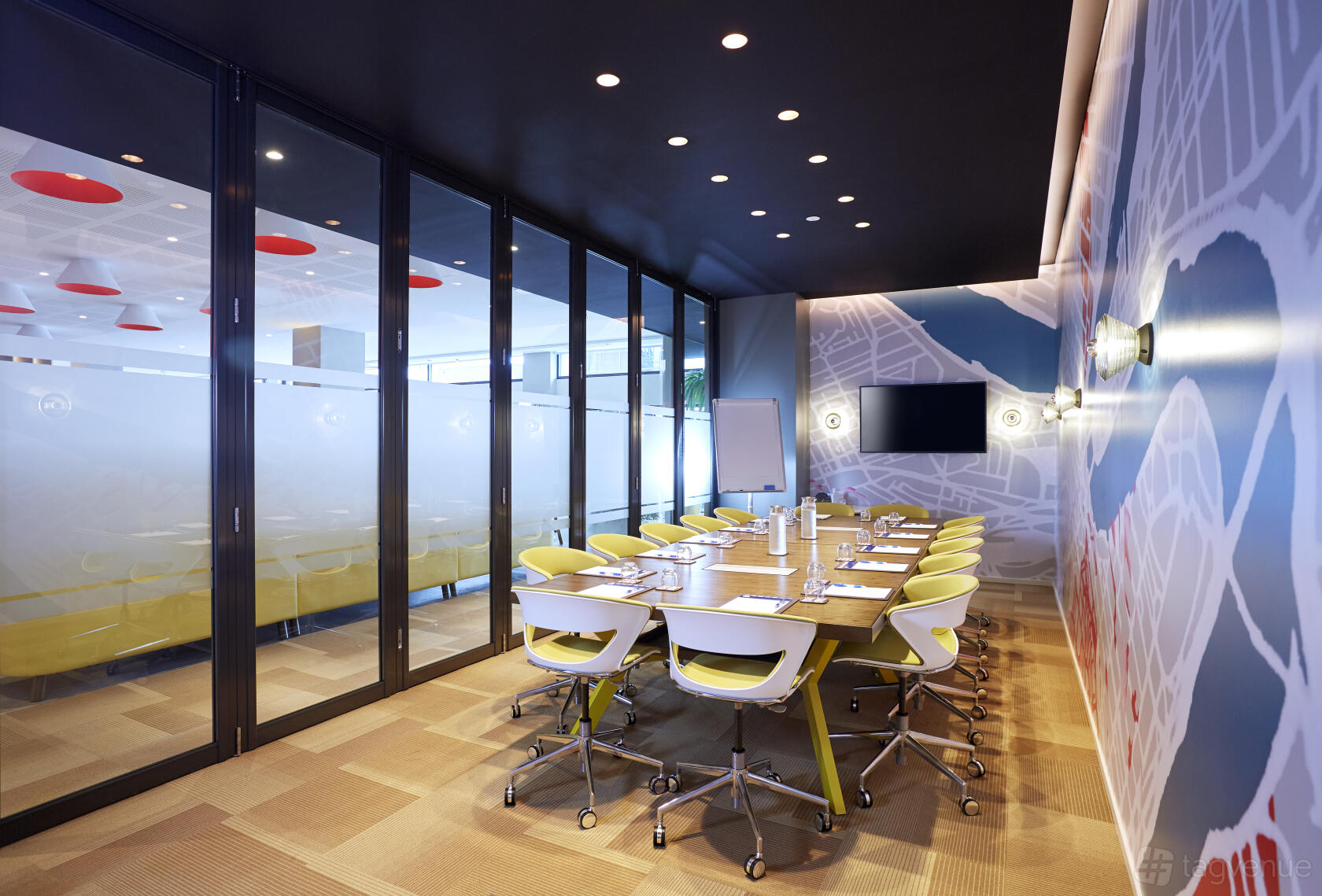 A meeting room with a long wooden table, ergonomic chairs, map wall graphics, and a wall-mounted screen at Holiday Inn Express Brisbane.