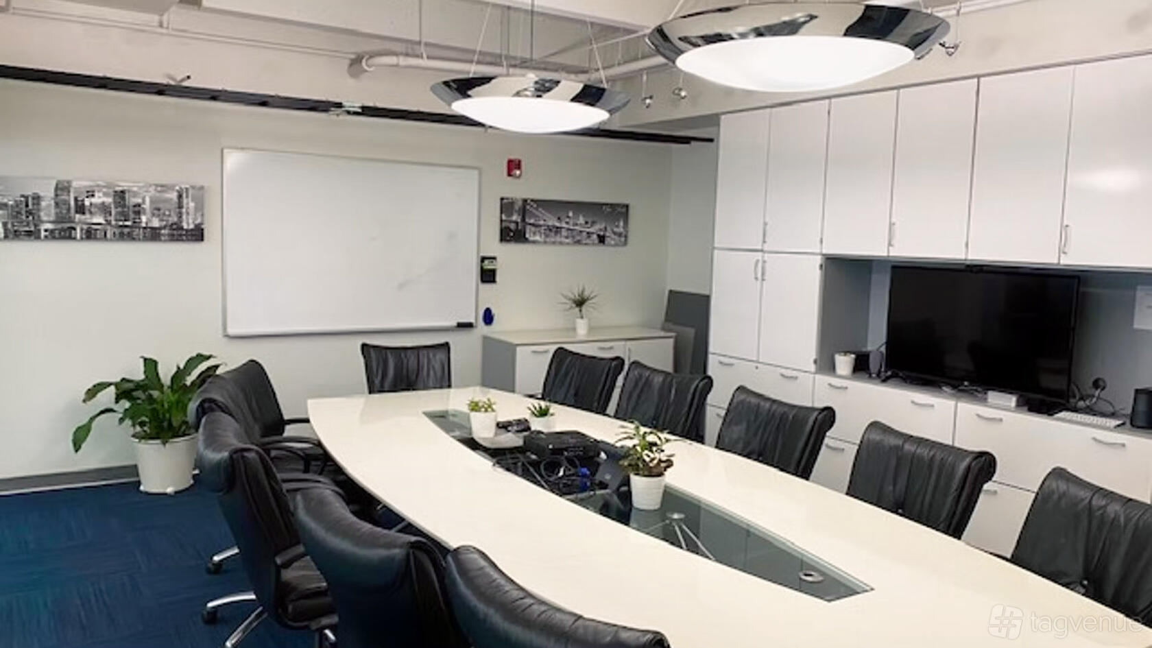 A meeting room with a long oval table, black leather chairs, white cabinets, and a wall-mounted whiteboard at Momentum Business Center.