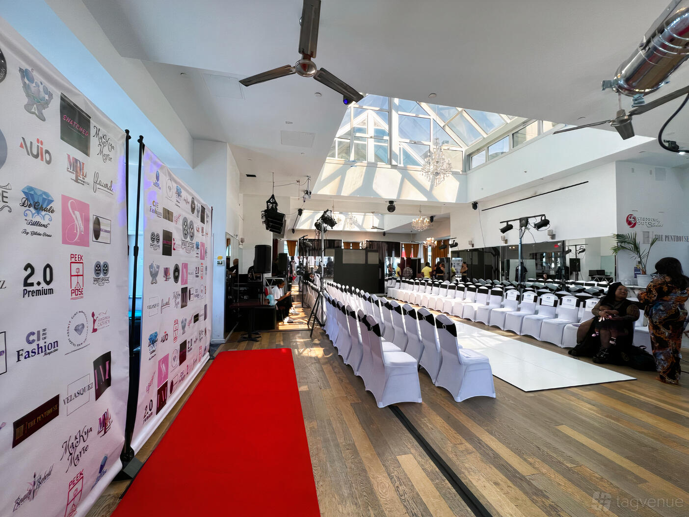 A function room with a glass ceiling, wooden floors, and rows of white chairs facing a runway at The Penthouse.