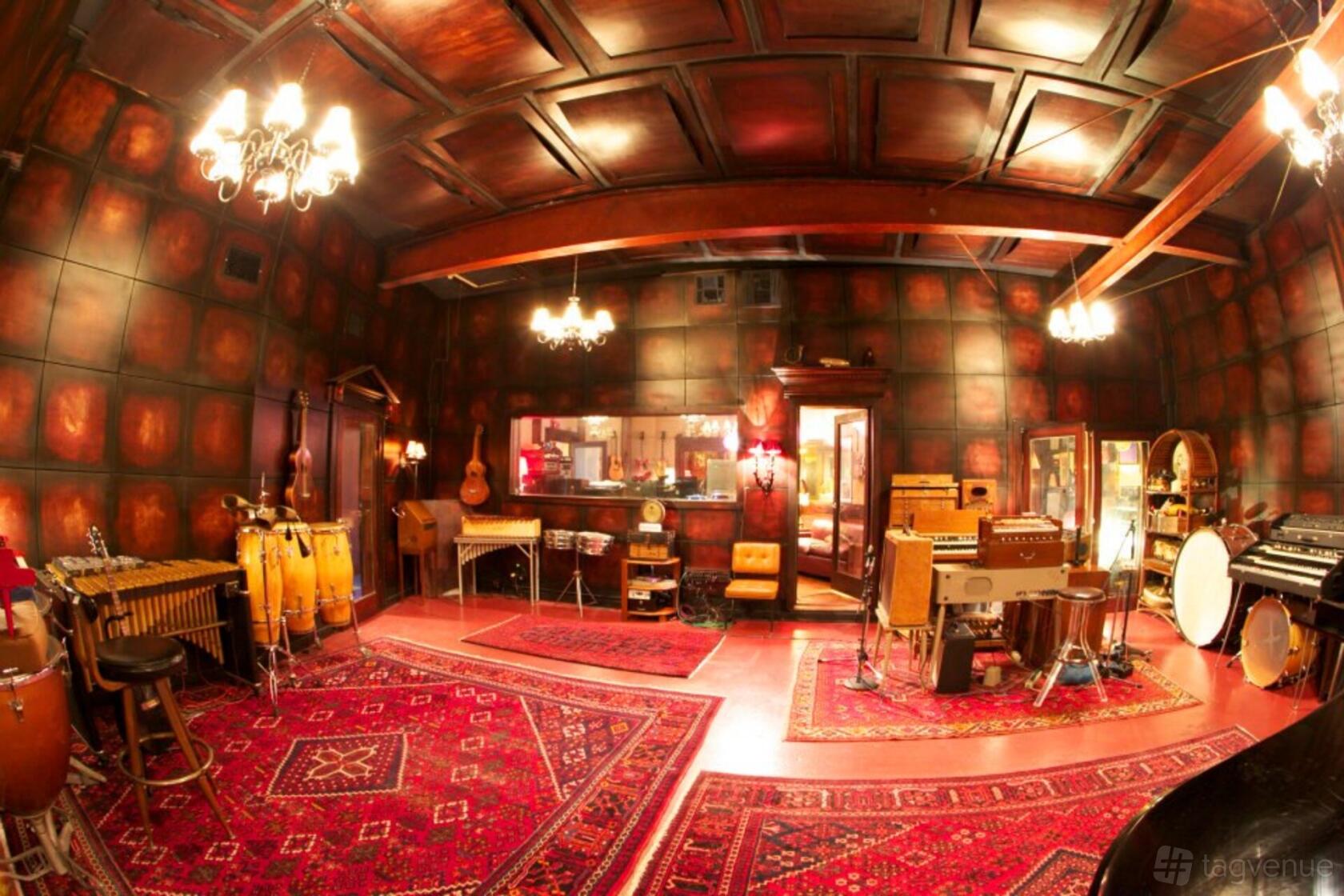 A recording studio with exposed wood beams, ornate rugs, vintage instruments, and wall-mounted acoustic panels at Matter Music.