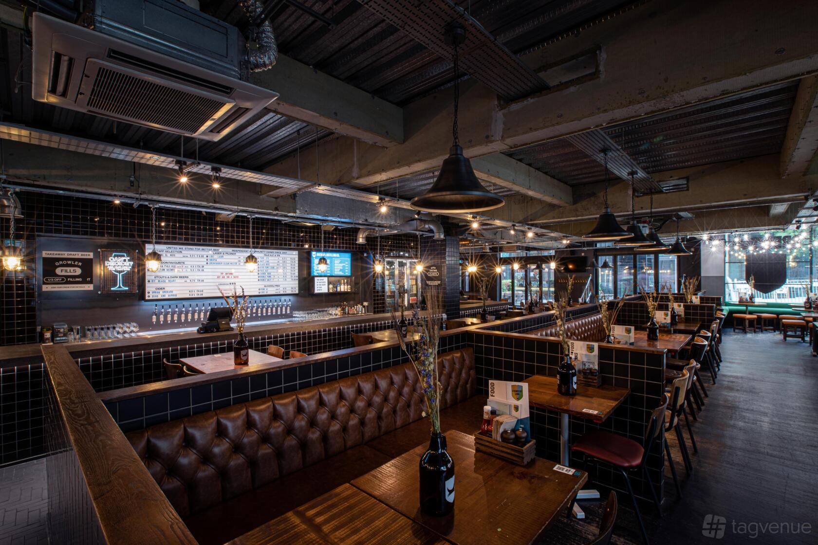 A restaurant with black tiled booths, pendant lighting, and exposed ceiling beams at BrewDog Chancery Lane.