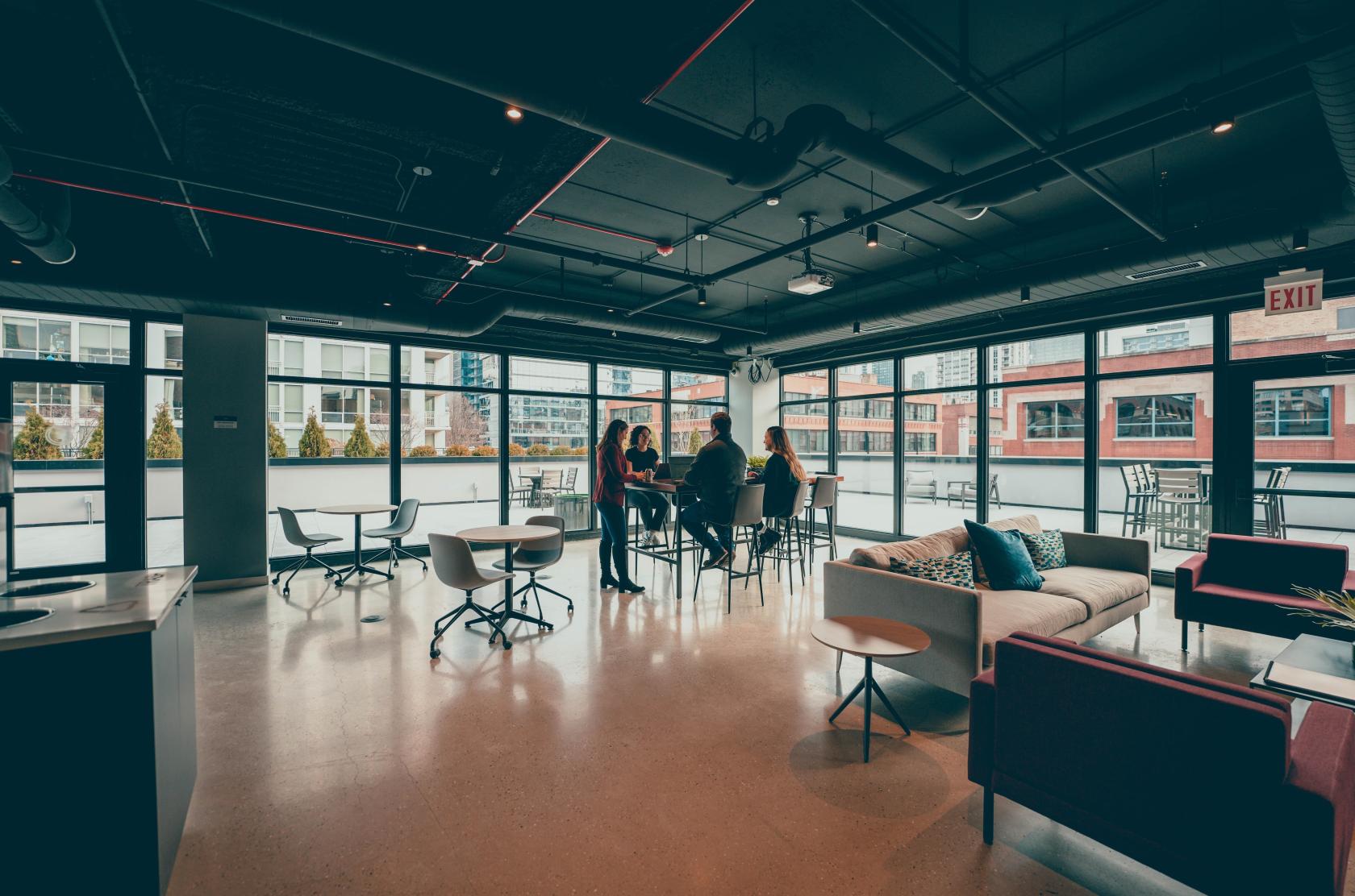 An office event space with floor-to-ceiling windows, lounge seating, and access to an outdoor terrace at Workbox - River North.
