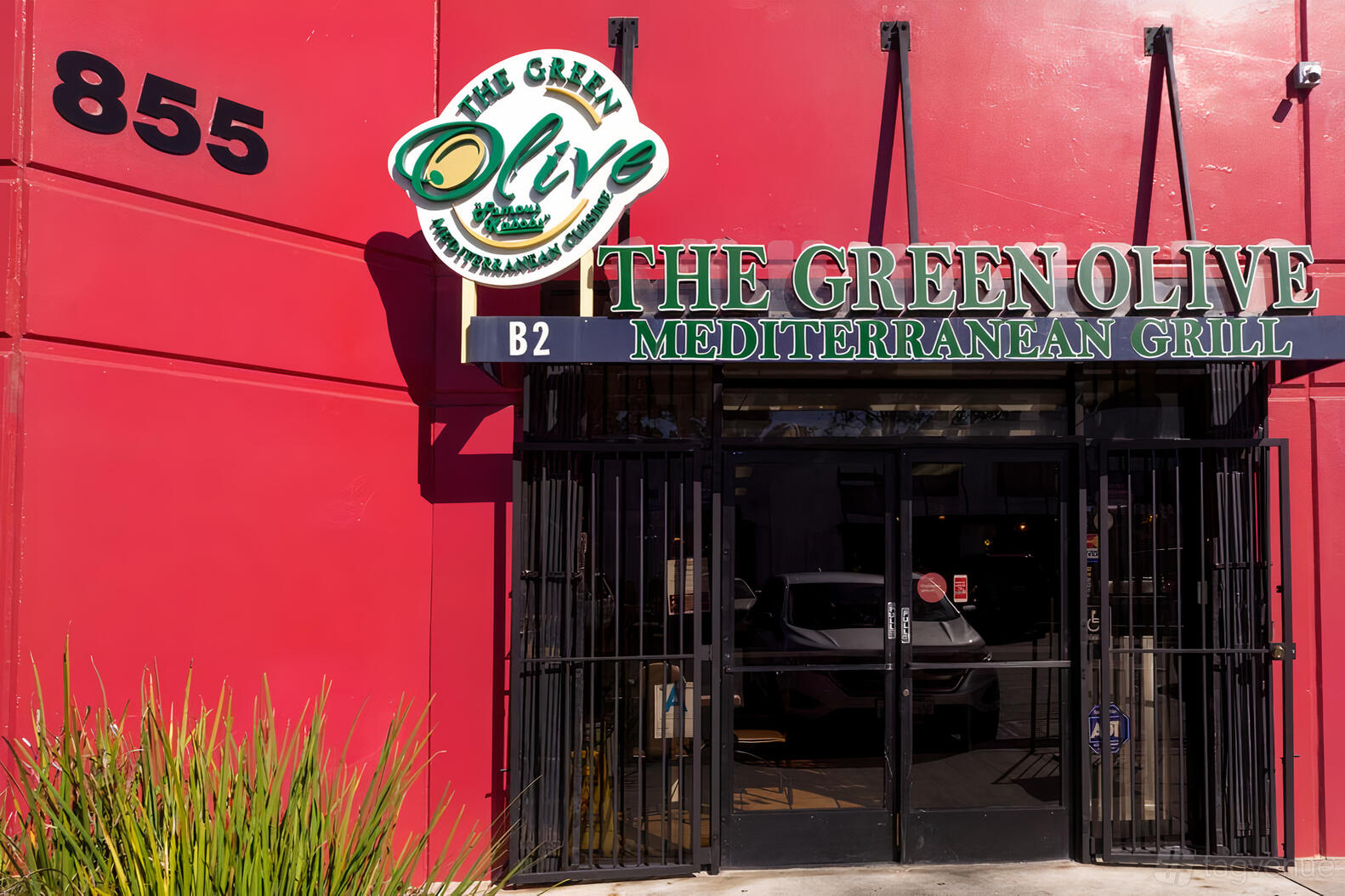 A restaurant exterior with red walls, iron gate doors, and green Mediterranean Grill signage at The Green Olive.