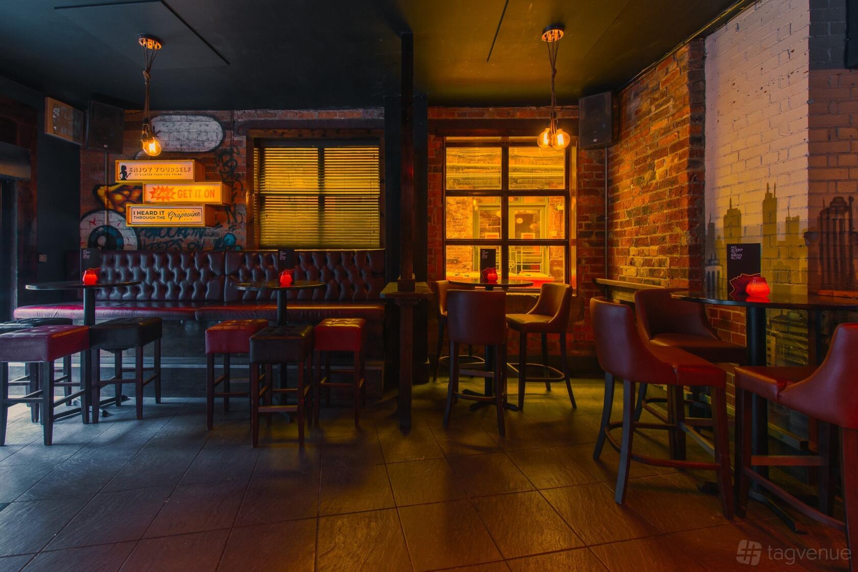 A cocktail bar with tufted leather seating, exposed brick walls, and pendant lighting at Brooklyn Bar.