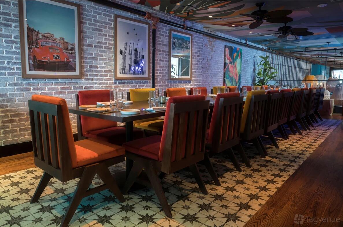 A dining room with patterned tile flooring, exposed brick walls, colorful chairs, and framed artwork at Centrada Cocina & Cocktails.