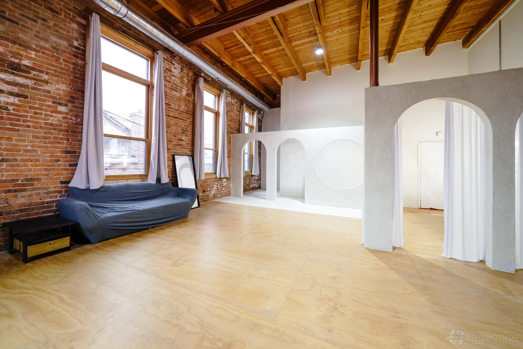 A photo studio with exposed brick walls, large windows, and a set with white arches at Chicago Studios.