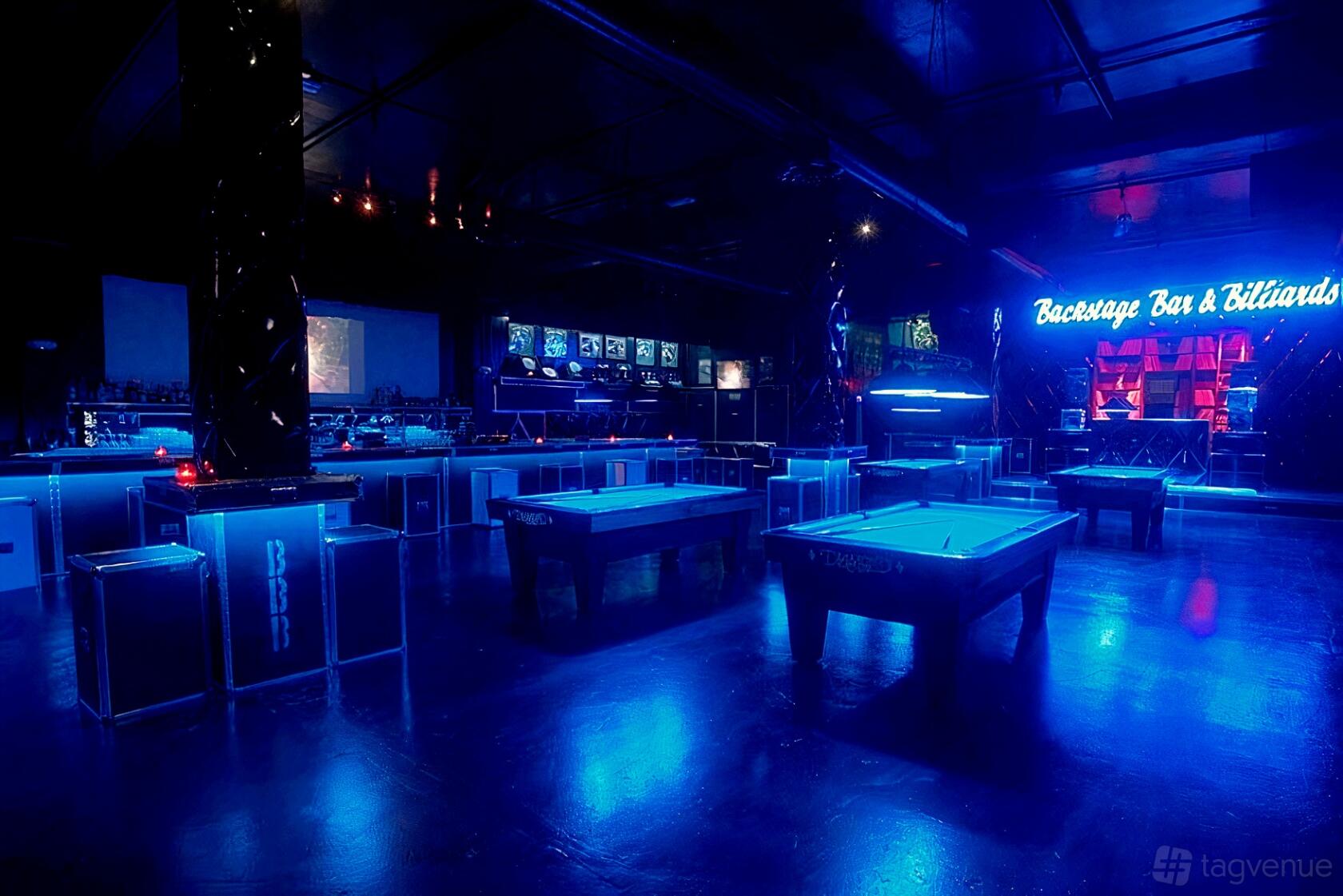 A bar with billiards tables, neon lighting, and illuminated signage at Backstage Bar & Billiards.
