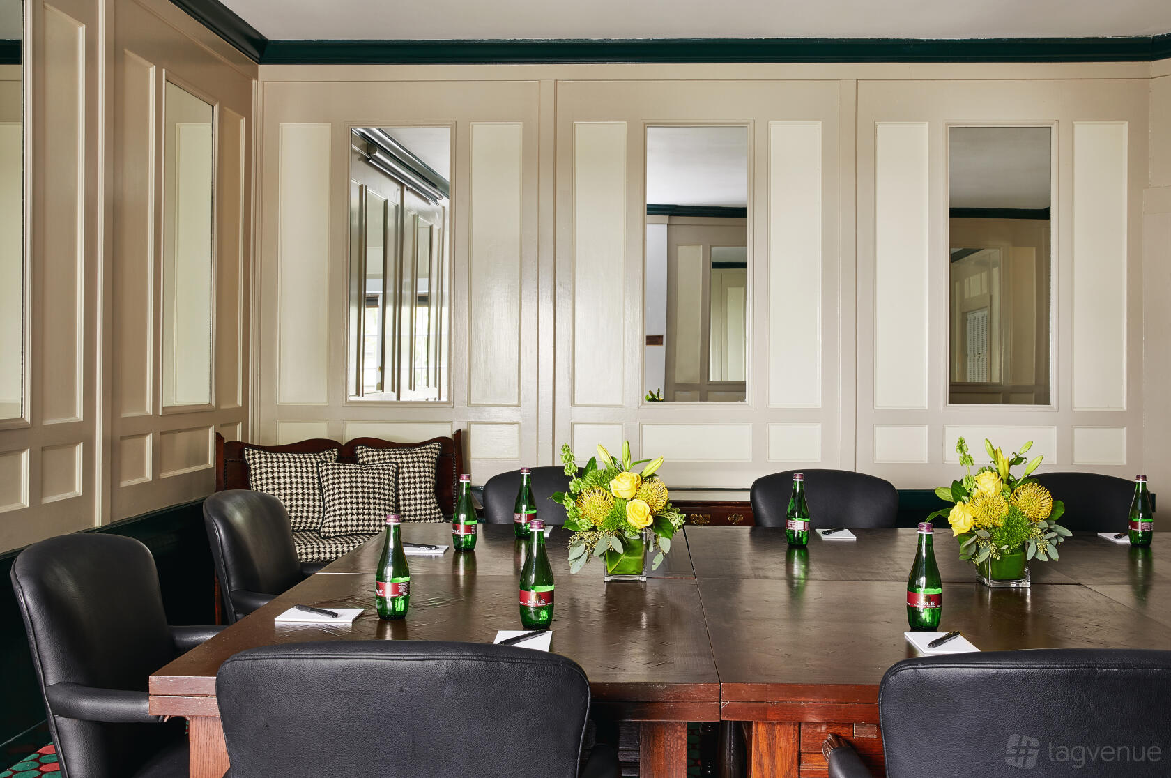 A meeting room with a dark wooden table, black chairs, bottled water, and floral centerpieces at White Swan Inn.
