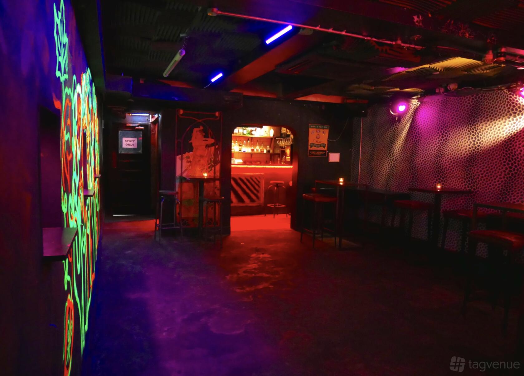 An event space in a cocktail bar with neon wall art, high tables, and a lit bar counter at The Ladybird Bar.