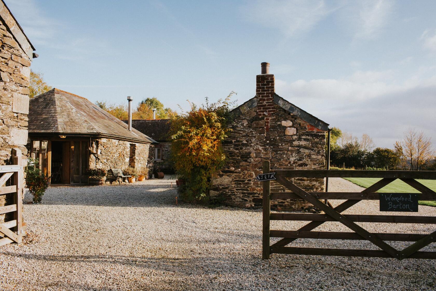 A countryside event space with stone buildings, gravel courtyard, and wooden gate at Wonwood Barton.