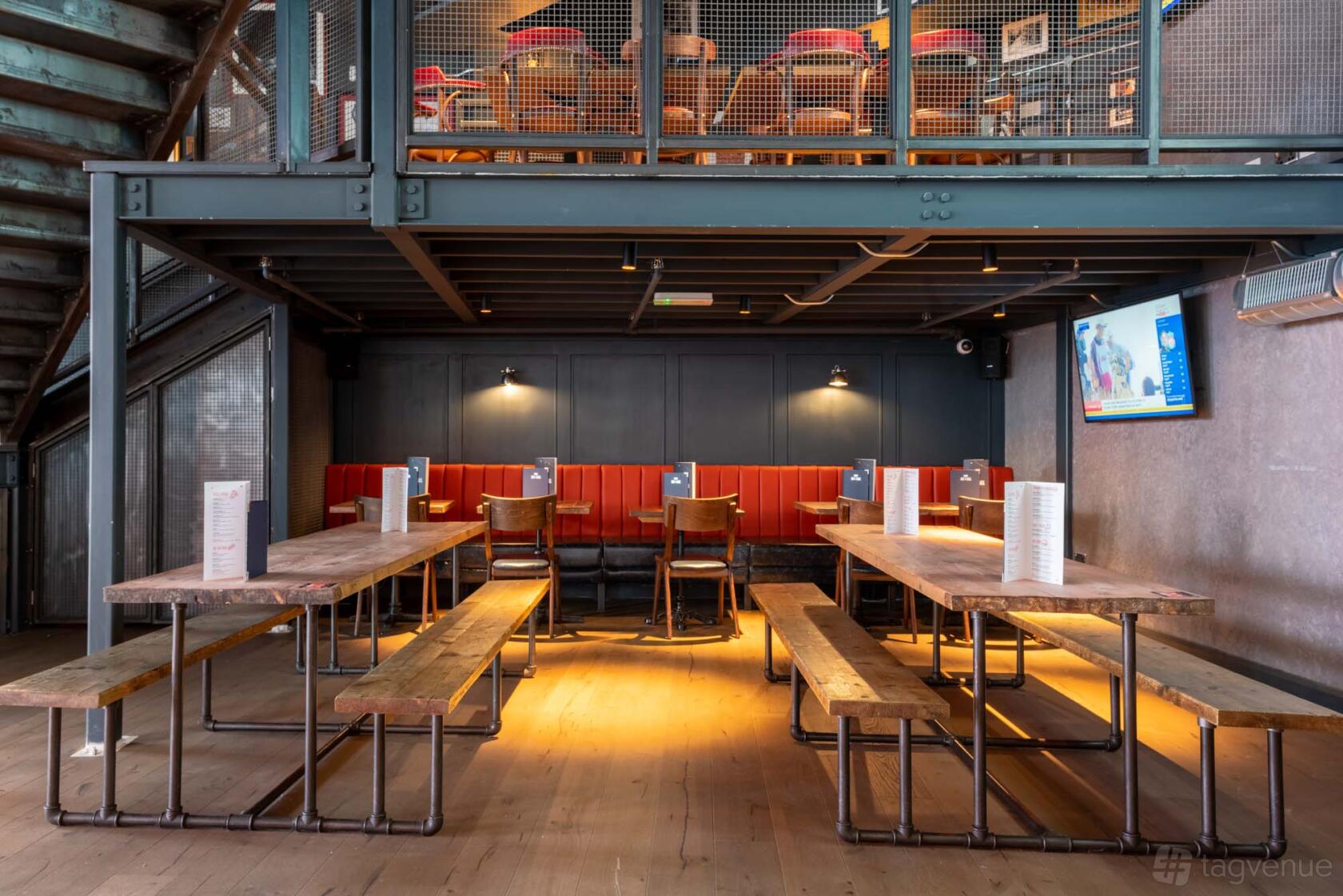 An event space with long wooden tables, red booth seating, and a wall-mounted TV at Bat & Ball.