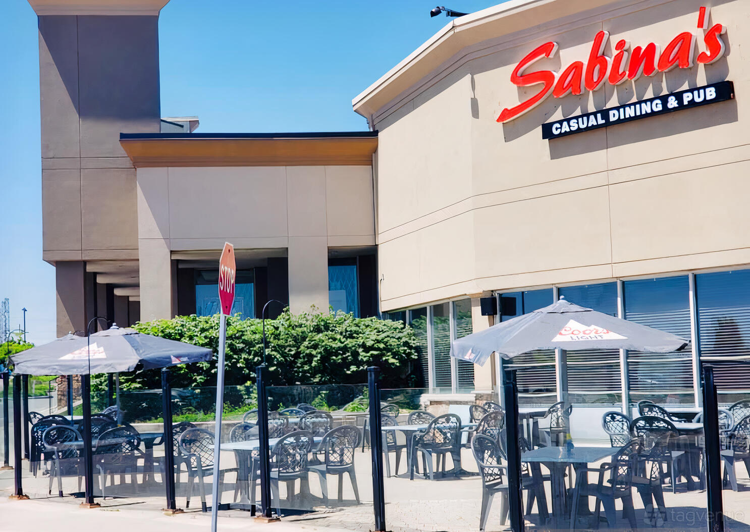A restaurant patio with black metal tables and chairs, shaded by umbrellas at Sabina's Casual Dining & Pub - Pickering.