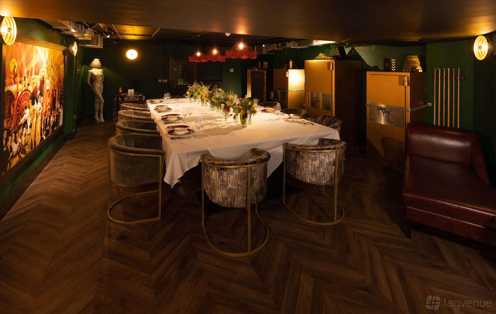 A hotel private dining room with a long table set for a formal meal, velvet chairs, wood flooring, and eclectic wall art at Hotel Gotham.