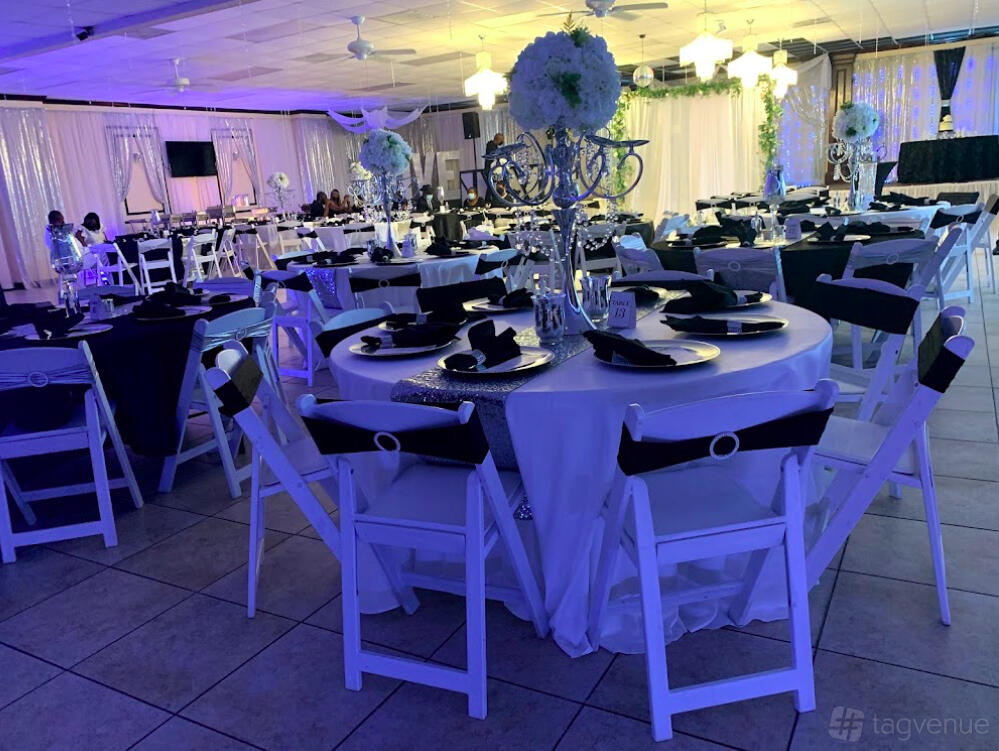 A banquet hall with round tables covered in white linens, black napkins, and floral centerpieces at Lily Reception Hall.