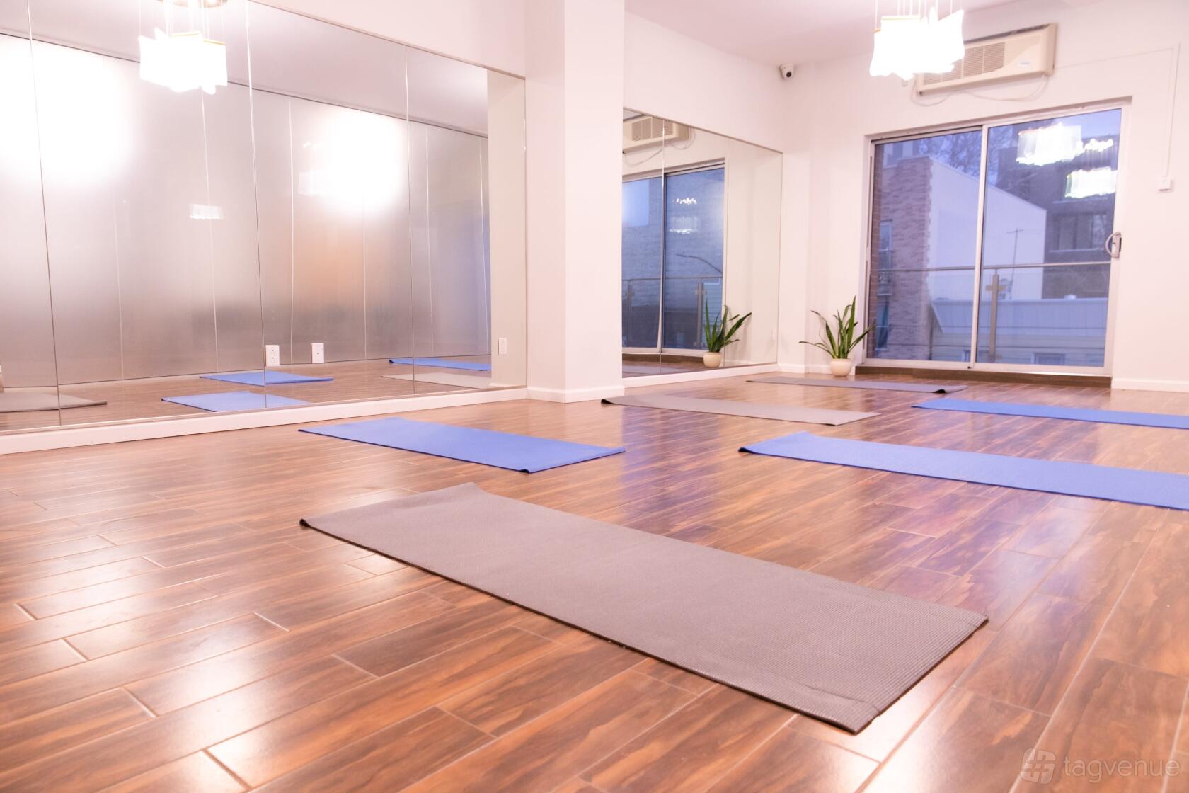 A fitness studio with large mirrors, wood floors, yoga mats, and natural light at The Modernist Hotel.