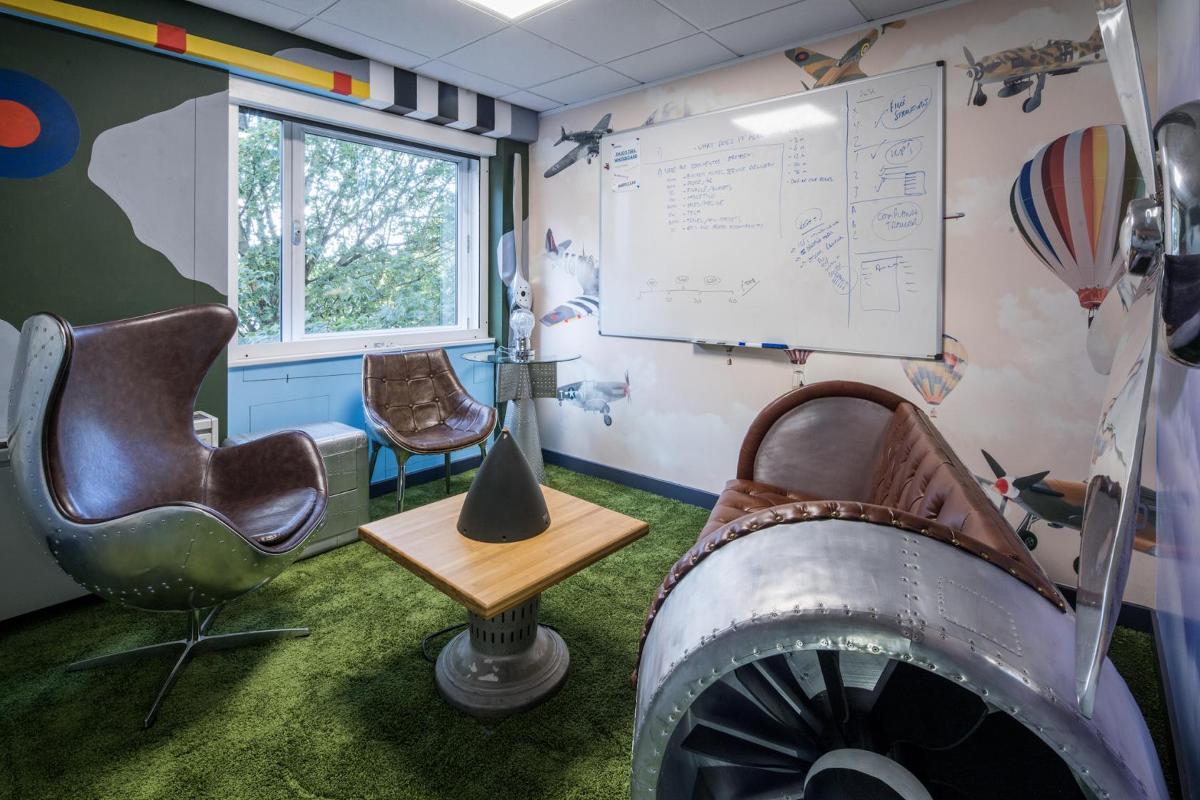 A meeting room with aviation-themed decor, leather chairs, and a wall-mounted whiteboard at DeskLodge House Bristol.