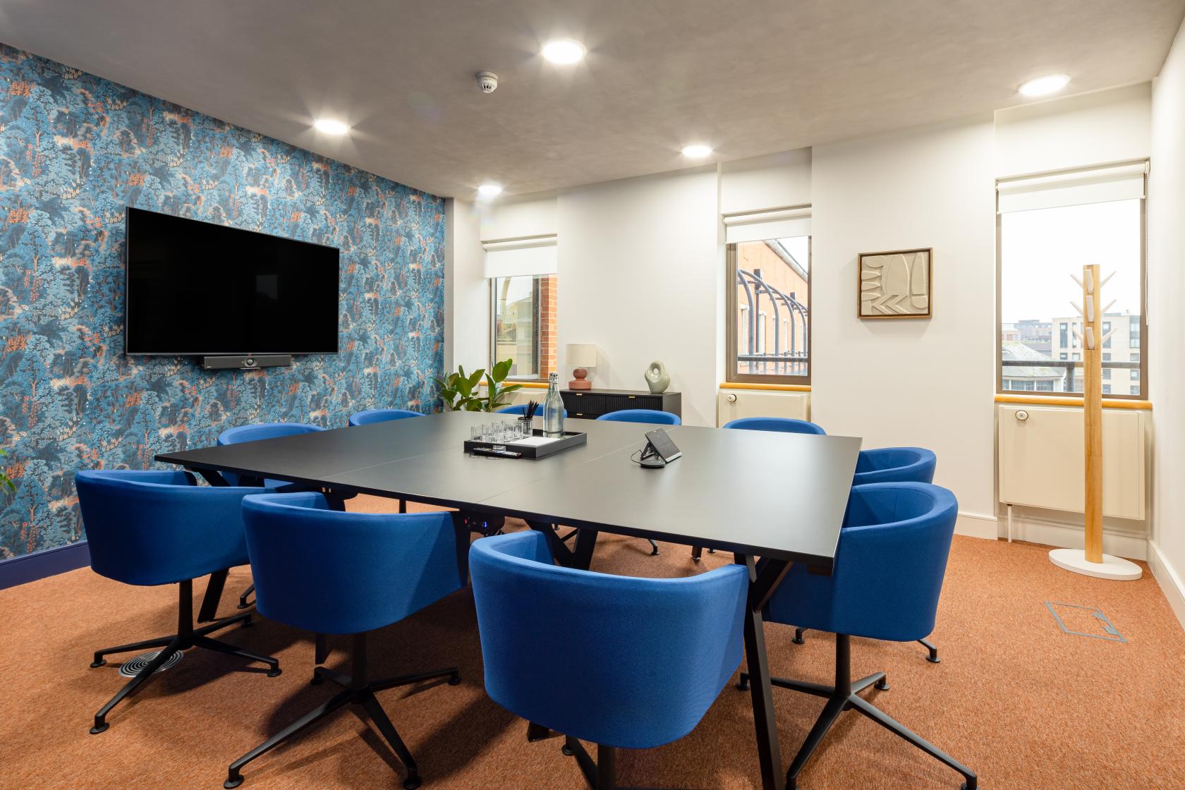 A meeting room with blue chairs around a rectangular table, patterned accent wall, and wall-mounted screen at Landmark: Bristol.