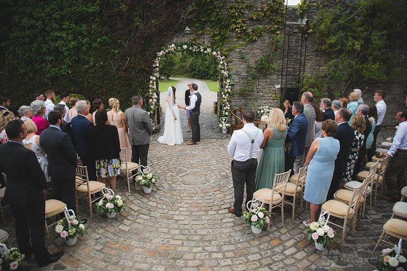 A castle courtyard with stone walls, cobblestone flooring, and an archway decorated with flowers at Walton Castle.