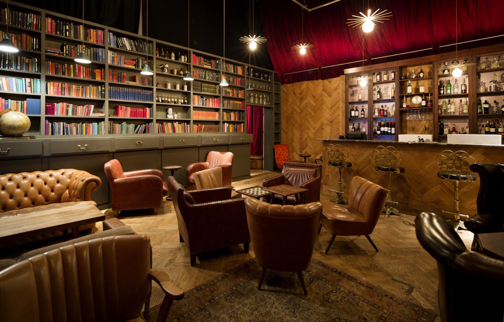 A lounge with leather armchairs, a vintage bar, parquet flooring, and wall-to-wall bookshelves at Benugo @ The BFI Southbank.