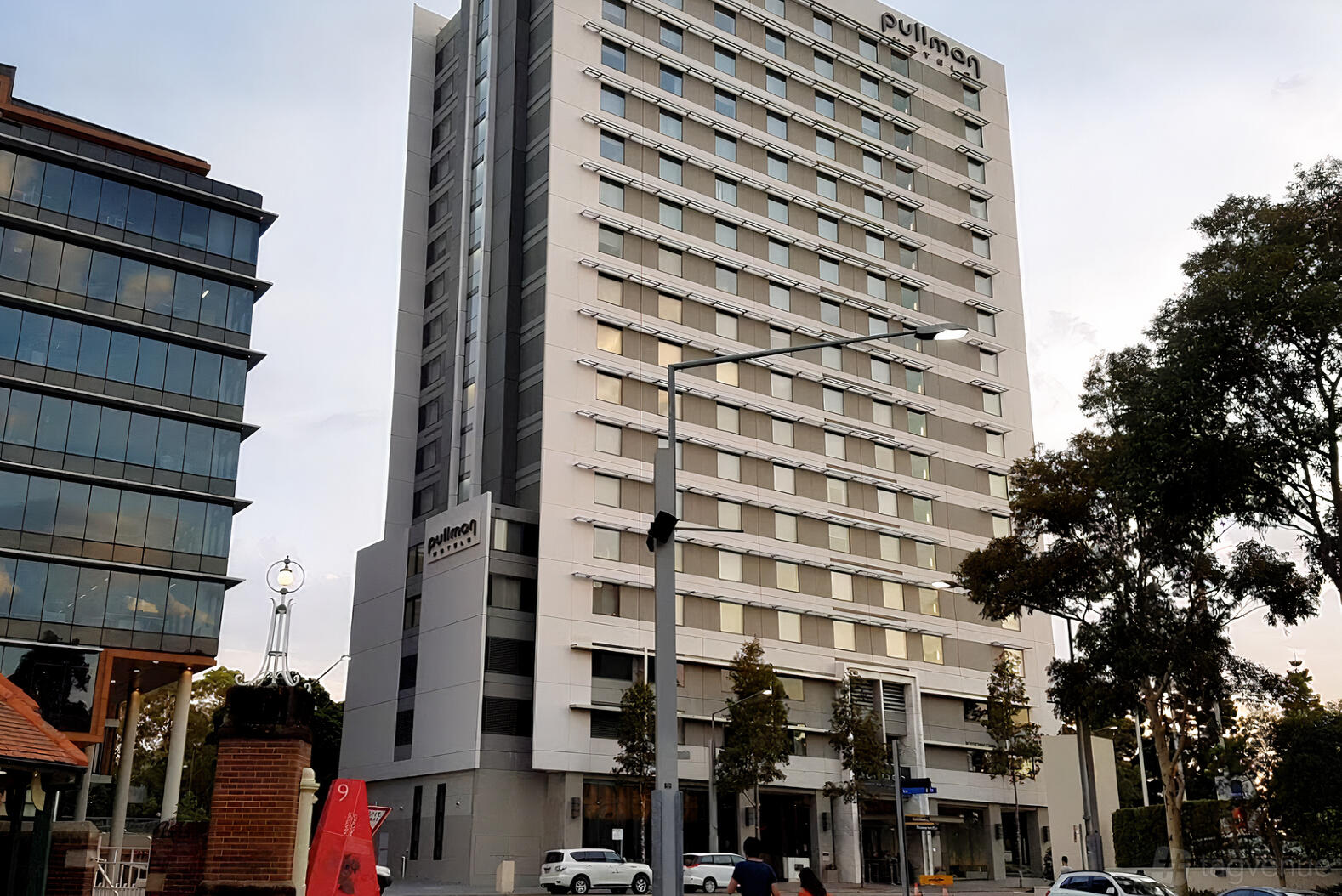 A modern hotel with a tall glass and concrete facade, large windows, and street trees at Pullman Sydney Olympic Park.