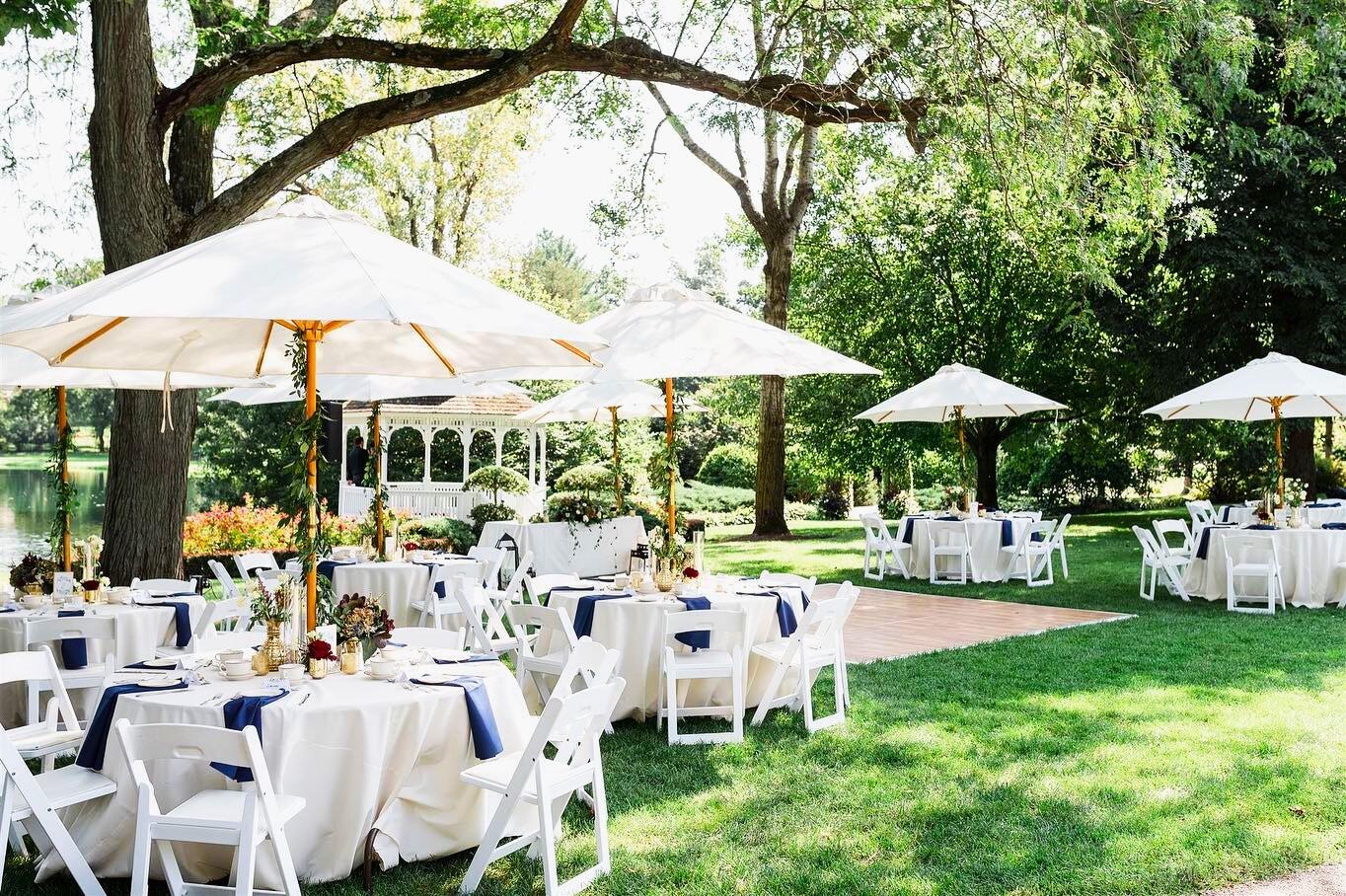 A garden venue with round tables covered in white linens, umbrellas, and a white gazebo at Wandering Tree Estate.