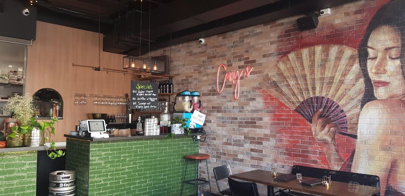 A bar with exposed brick walls, a neon sign, green-tiled bar counter, and wall art at Cony's.