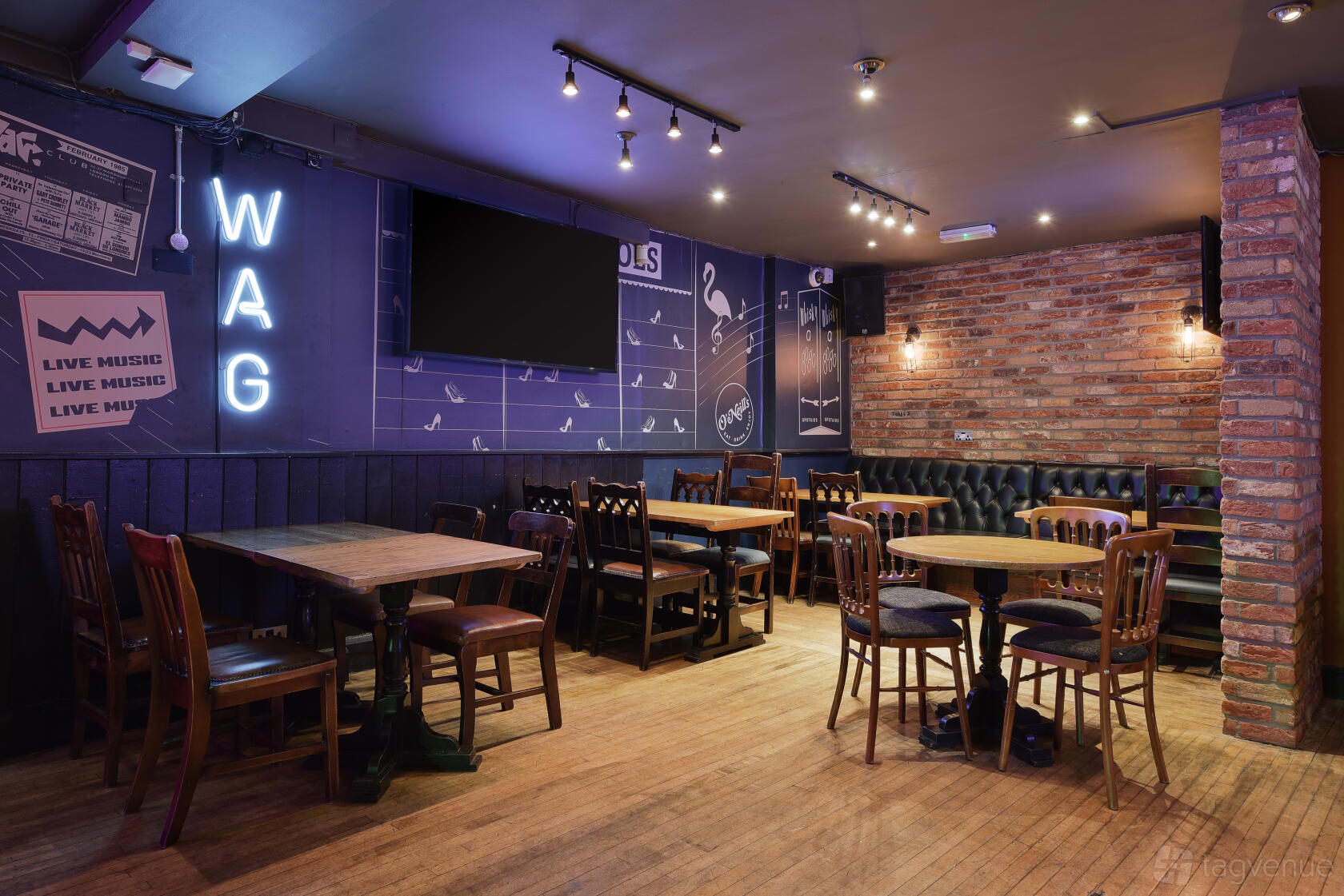 An event space in a pub with exposed brick walls, neon signage, and wooden tables at O'Neill's Wardour Street.