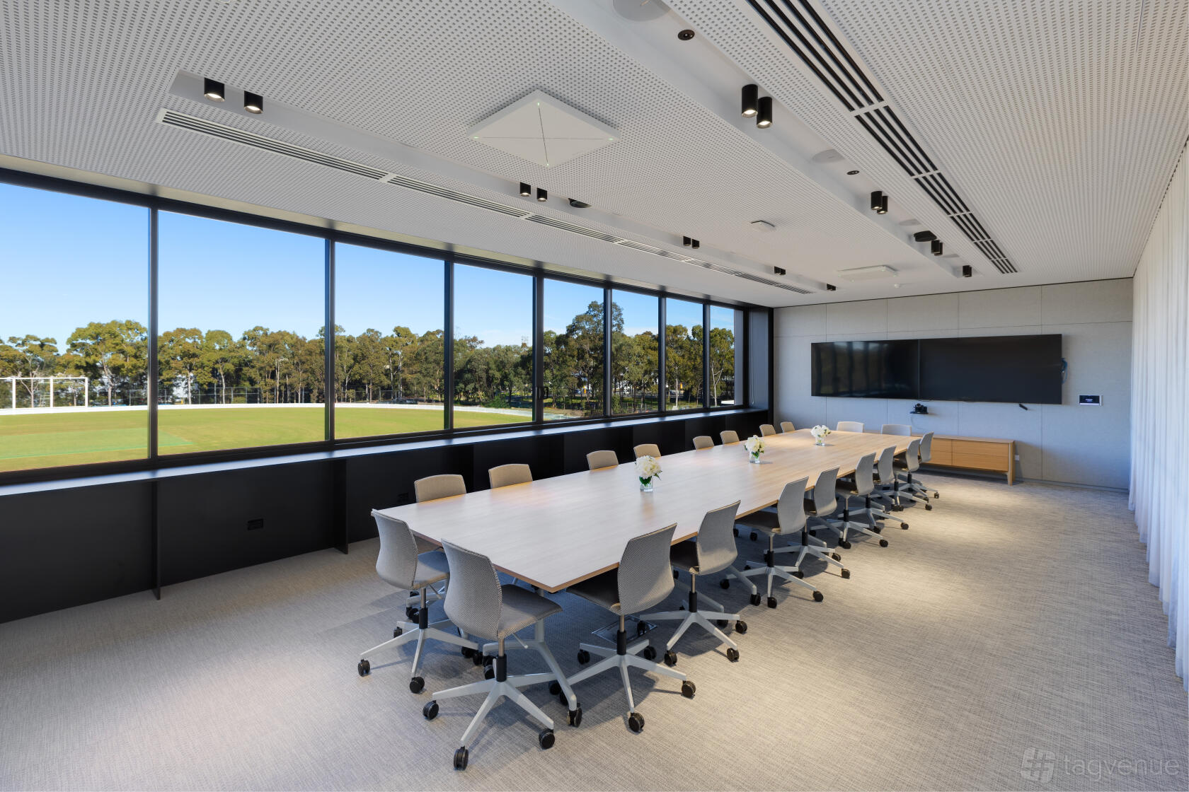 A boardroom with floor-to-ceiling windows, rectangular table, and large wall-mounted screen at Cricket Central.