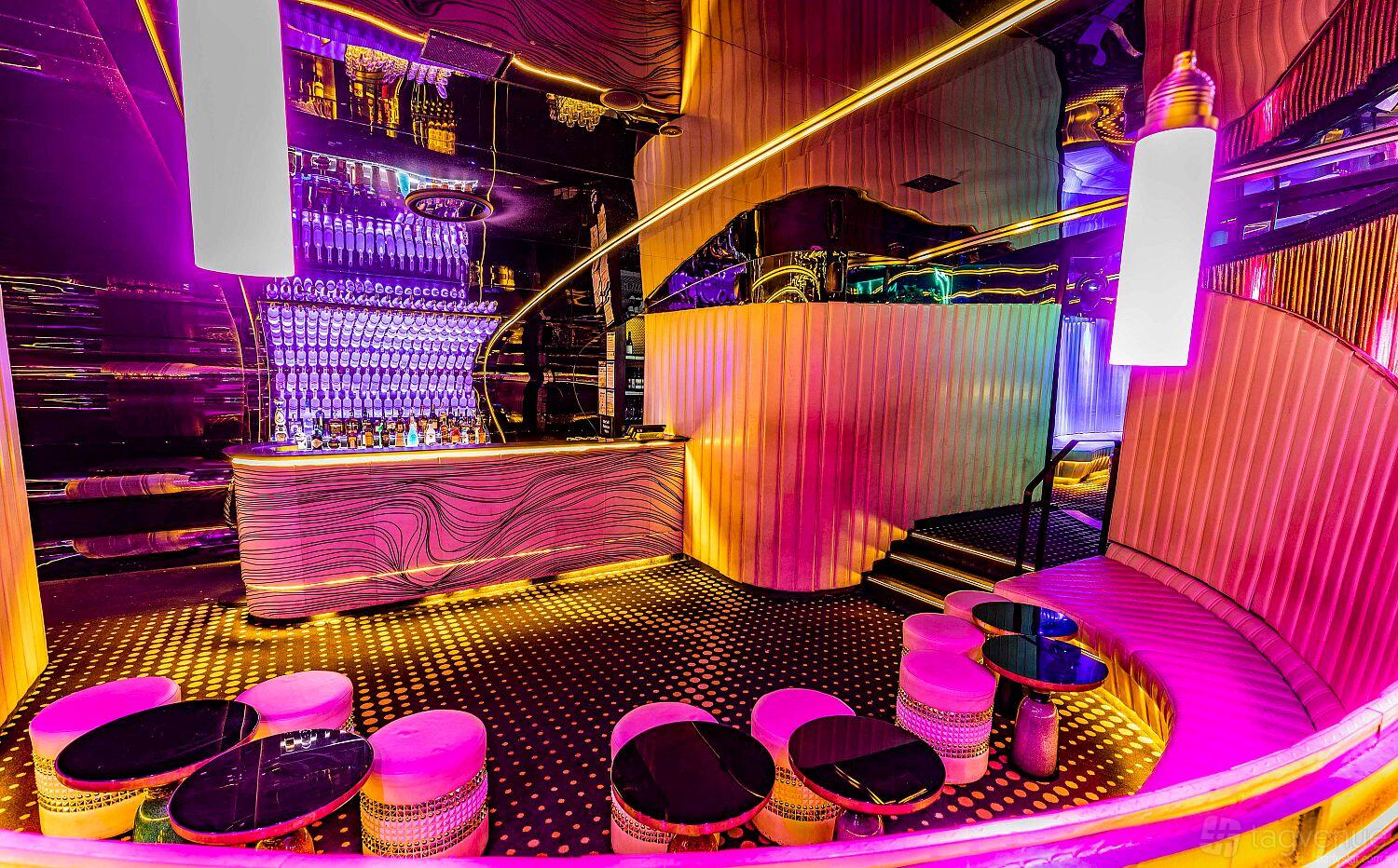 A nightclub with neon lighting, mirrored walls, and round seating booths at Bond Melbourne.