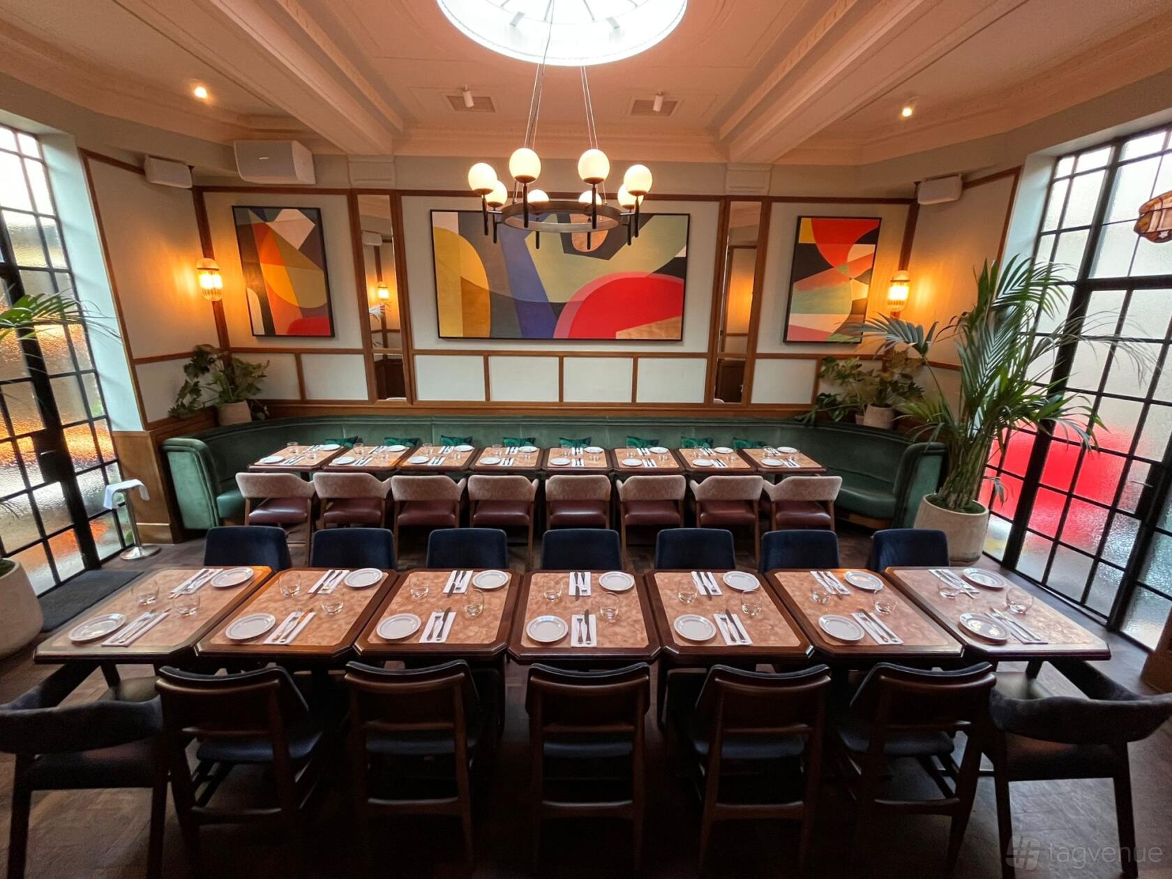 A dining room with long wooden tables, dark chairs, colorful abstract art, and frosted glass panels at Tutto.
