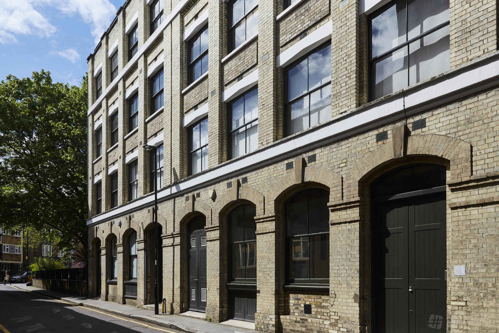 A brick apartment building with large arched windows and a tree-lined street at Sizona Location.