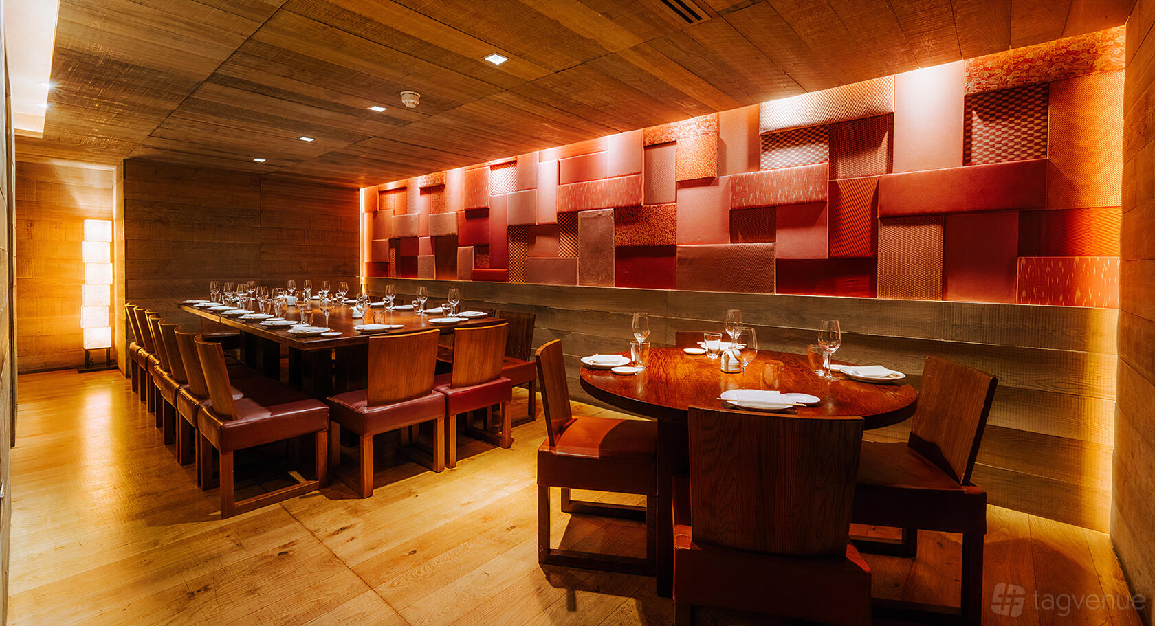 A dining room with wooden tables, leather chairs, and a textured red accent wall at Roka Mayfair.