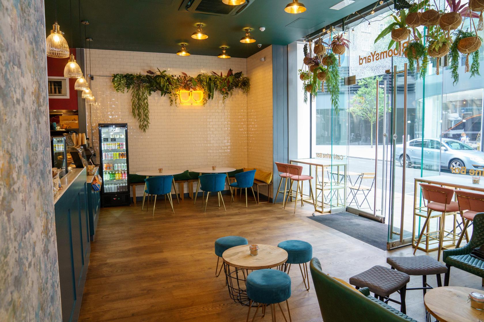 A cafe with wooden floors, botanical accents, pendant lighting, and window seating at BloomsYard Marble Arch.