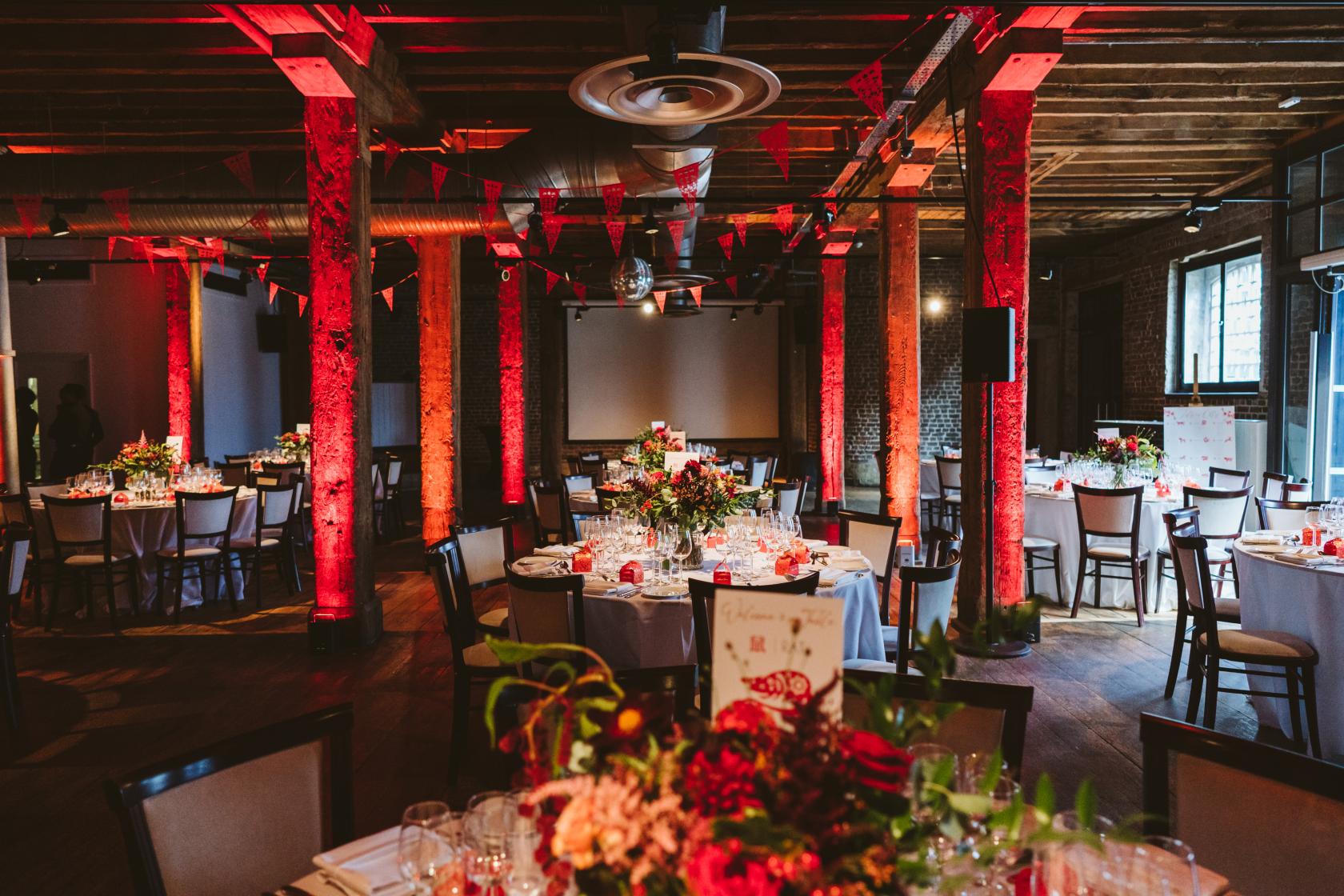 An event space with exposed brick pillars, wooden beams, and round banquet tables at London Museum Docklands.