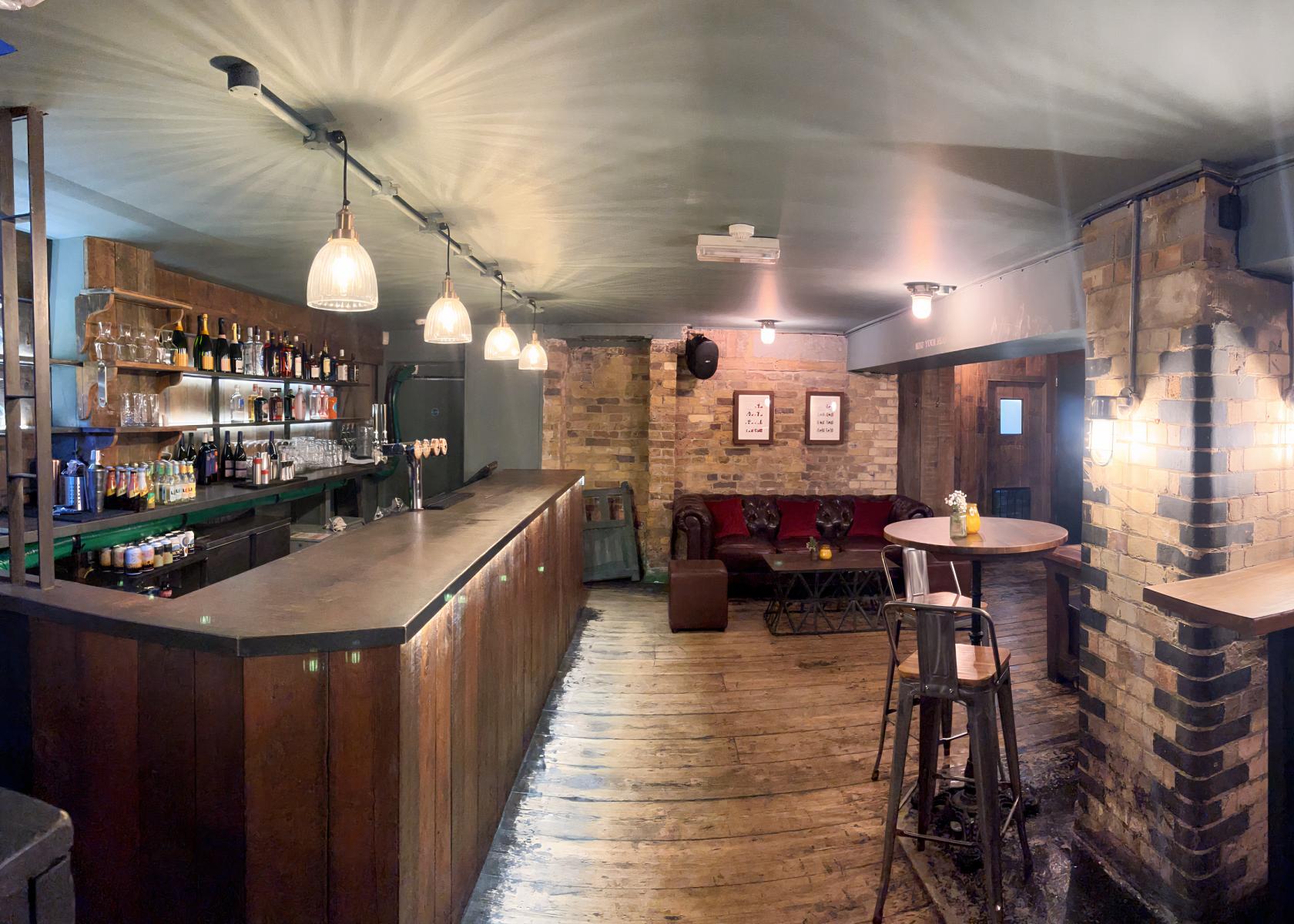 A basement pub with exposed brick walls, wooden floors, a long bar, and lounge seating at The Clerkenwell Tavern.