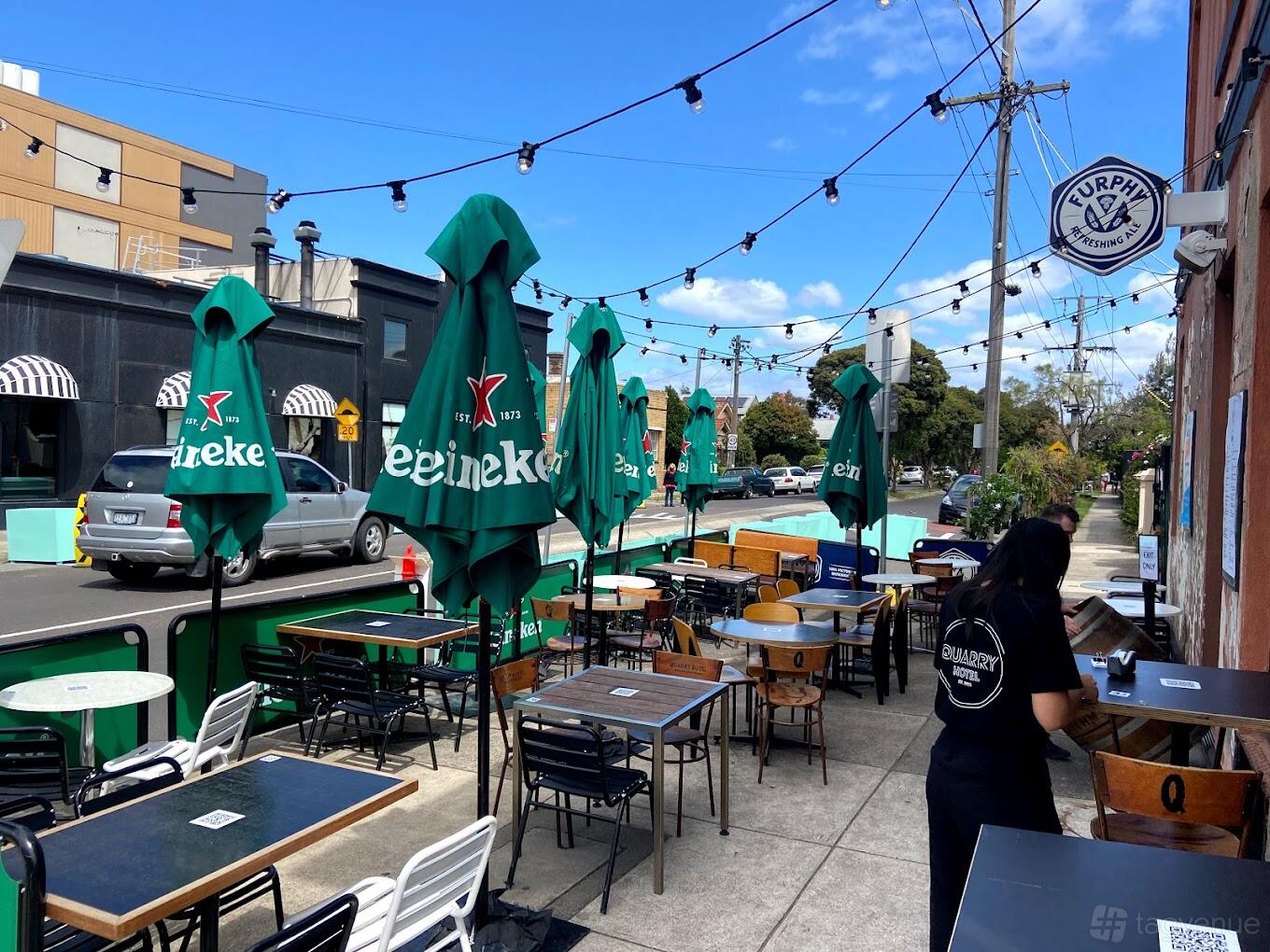 An outdoor pub area with string lights, green Heineken umbrellas, and mixed seating at The Quarry Hotel.