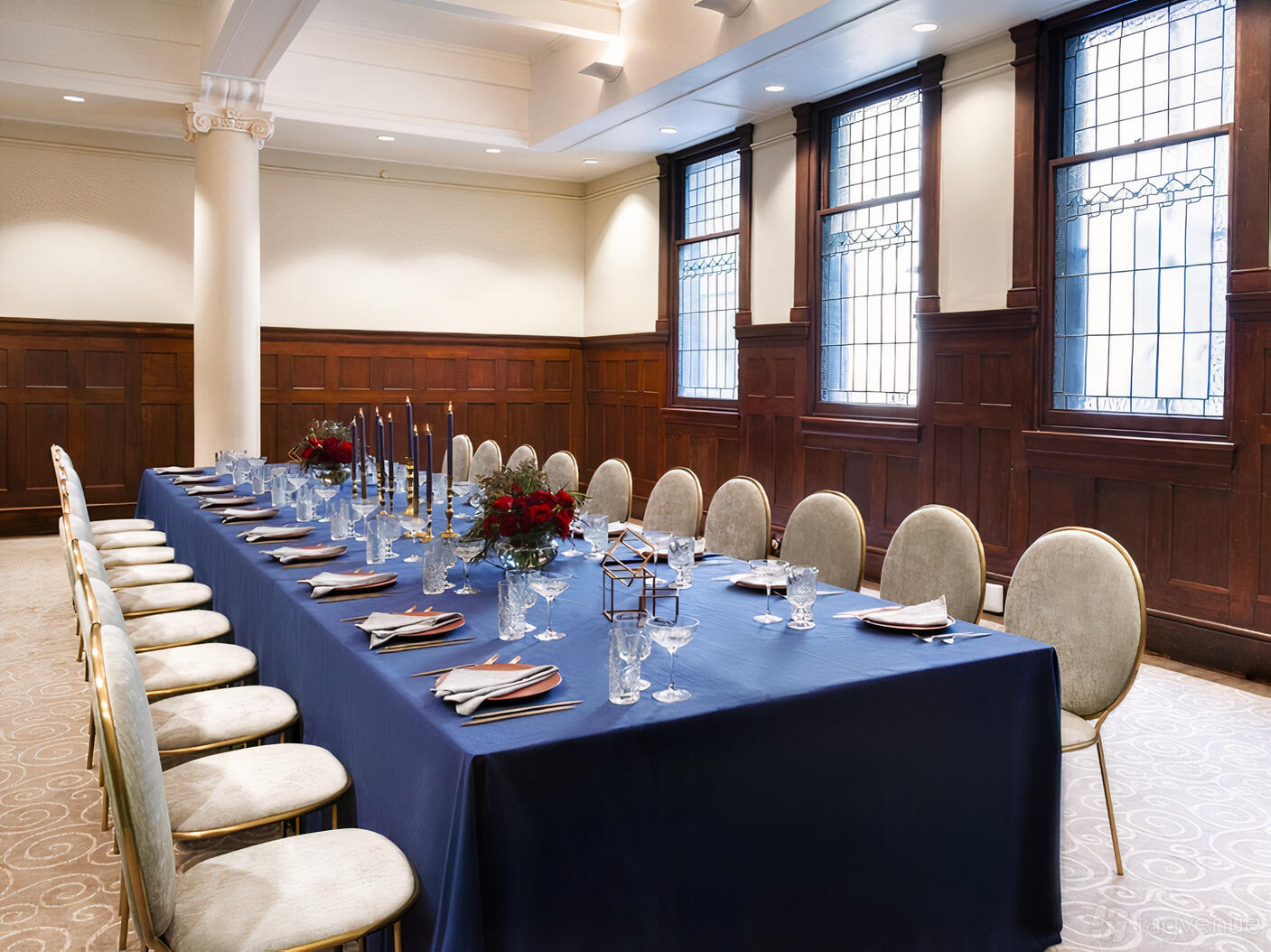 A hotel meeting room with stained glass windows, wood paneling, and a long table set with blue linens at Rendezvous Hotel Melbourne.