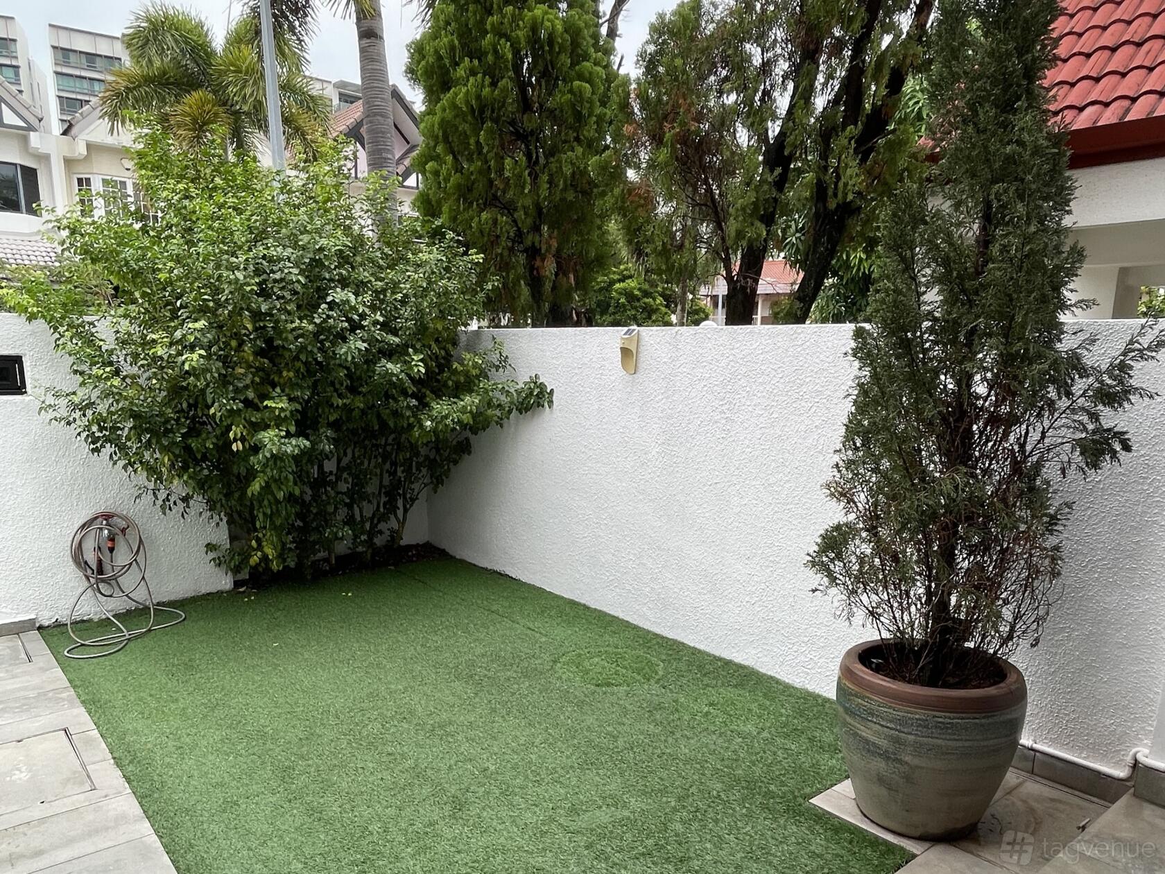 An apartment courtyard with artificial grass, white walls, and potted trees at White Modern Minimalist Landed Home.
