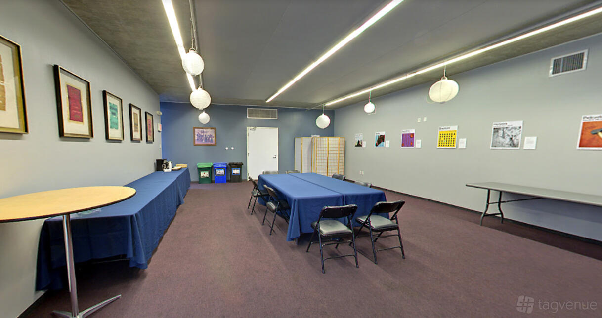 A meeting room with folding chairs, rectangular tables, framed wall art, and globe pendant lights at Congregation Beth Sholom.