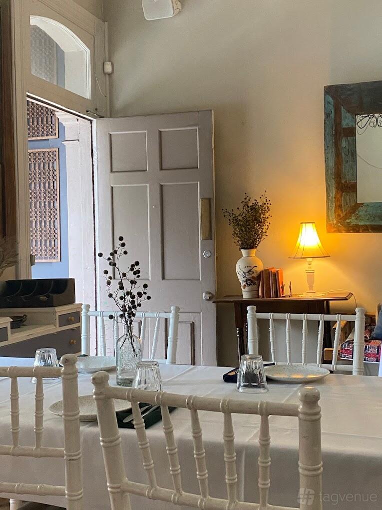 A restaurant with white chairs, a table set with glassware, and a side table with a lit lamp and decorative vase at House Bar&Bistrot.