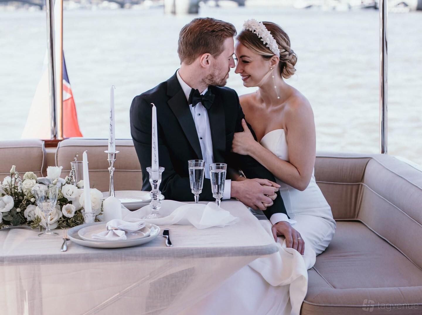 A yacht with a formal dining table set with white linens, candles, and a floral centerpiece at Thames Limo.