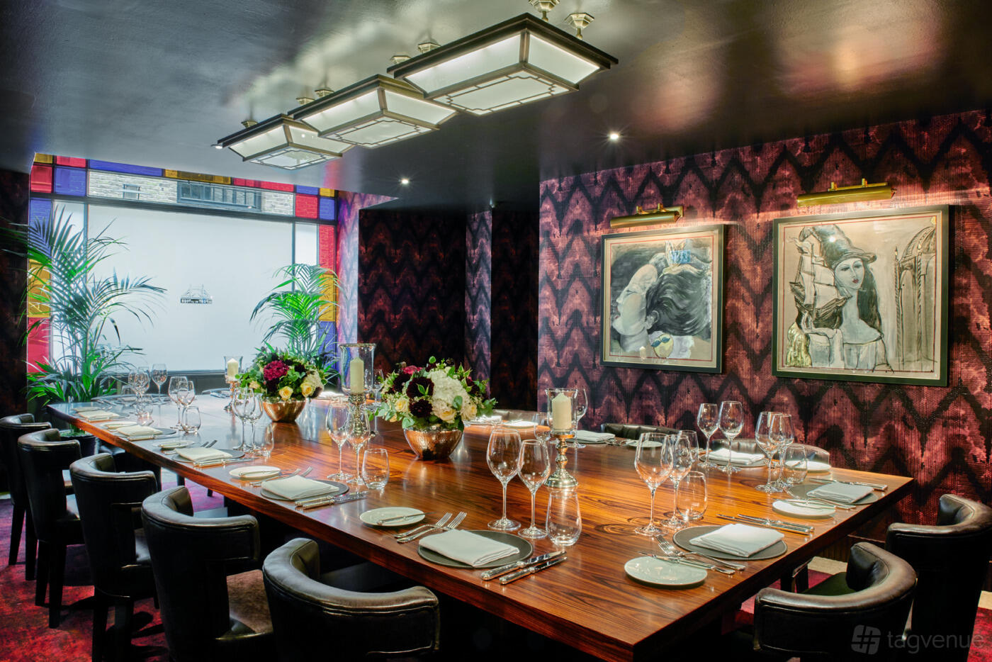 A dining room with a long wooden table, leather chairs, floral centerpieces, and modern art at Le Pont de la Tour.
