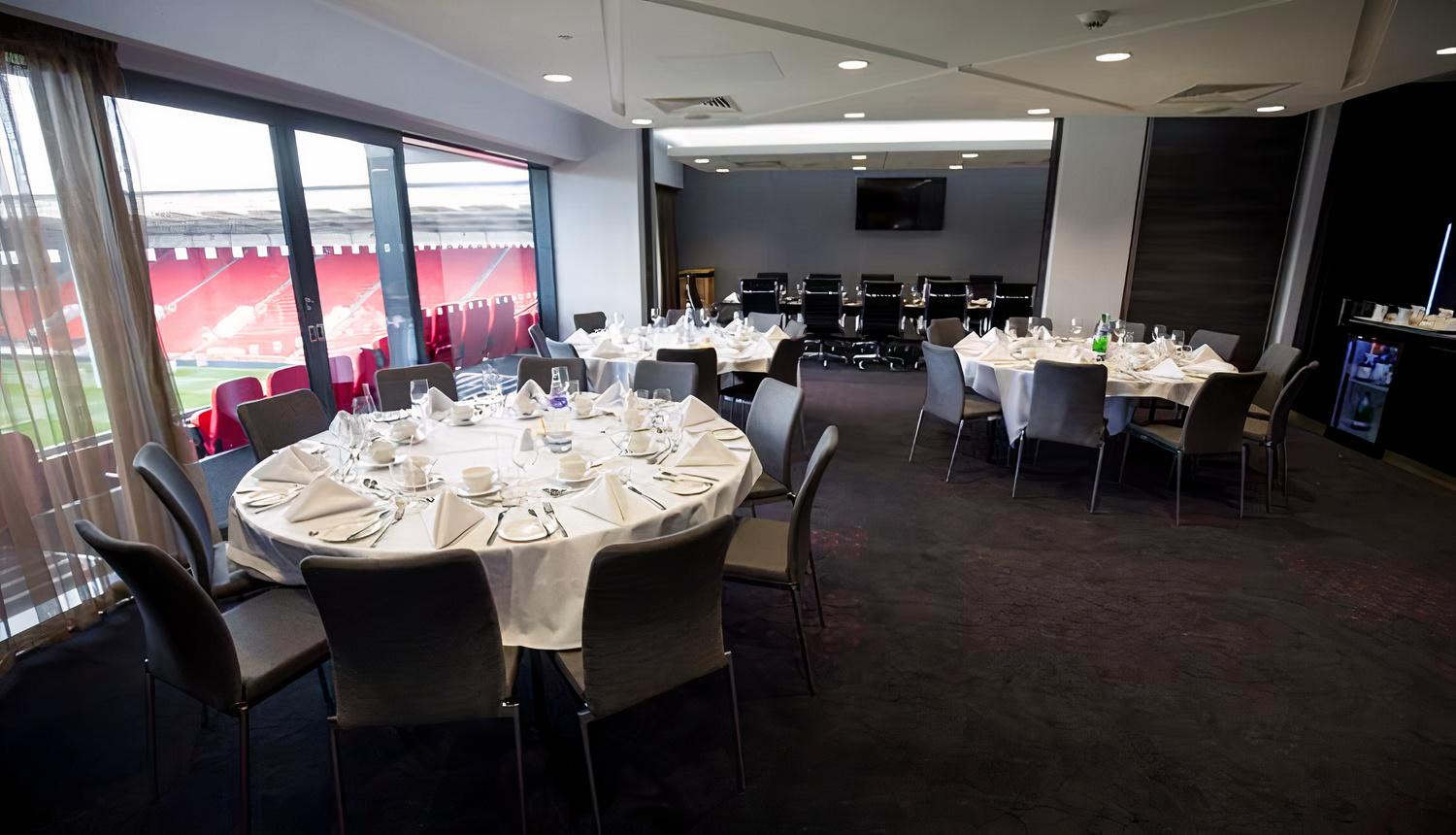 A lounge with round tables dressed in white linens and stadium views through large windows at Ashton Gate Stadium.