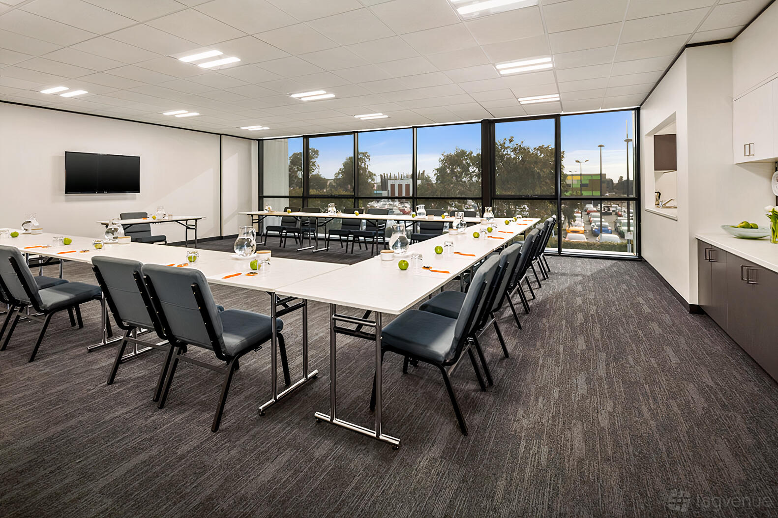 A conference room with U-shaped tables, cushioned chairs, floor-to-ceiling windows, and a wall-mounted screen at Uni Hill Conference Centre.