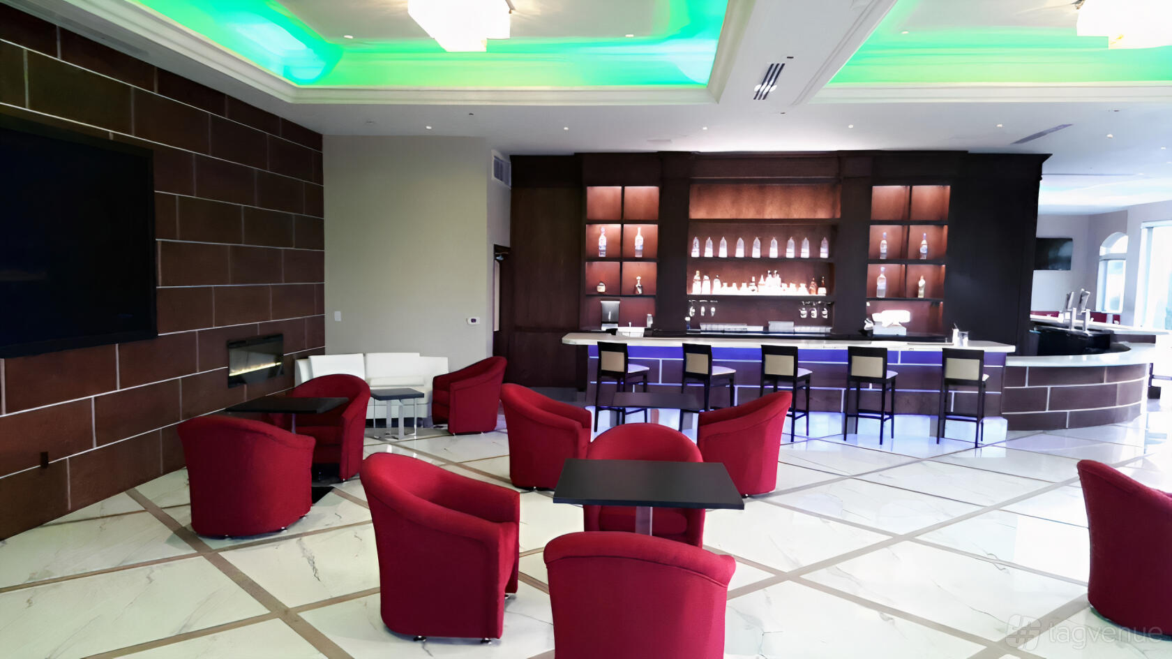 An event space in a fitness studio with red armchairs, a marble floor, and a backlit bar at South End Racquet And Heath Club.